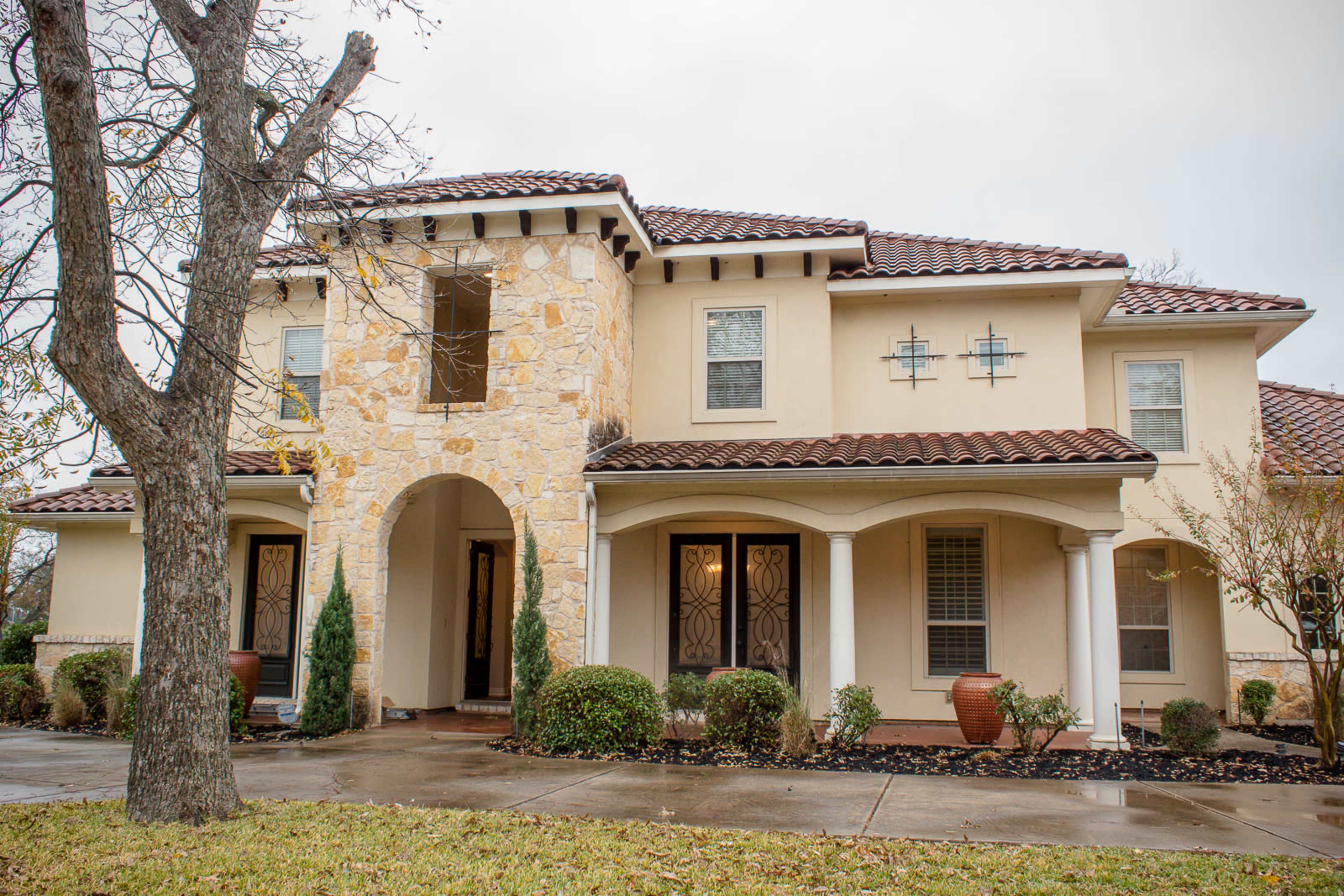 A two-story house with a stone and stucco facade, a tiled roof, and a covered front porch.