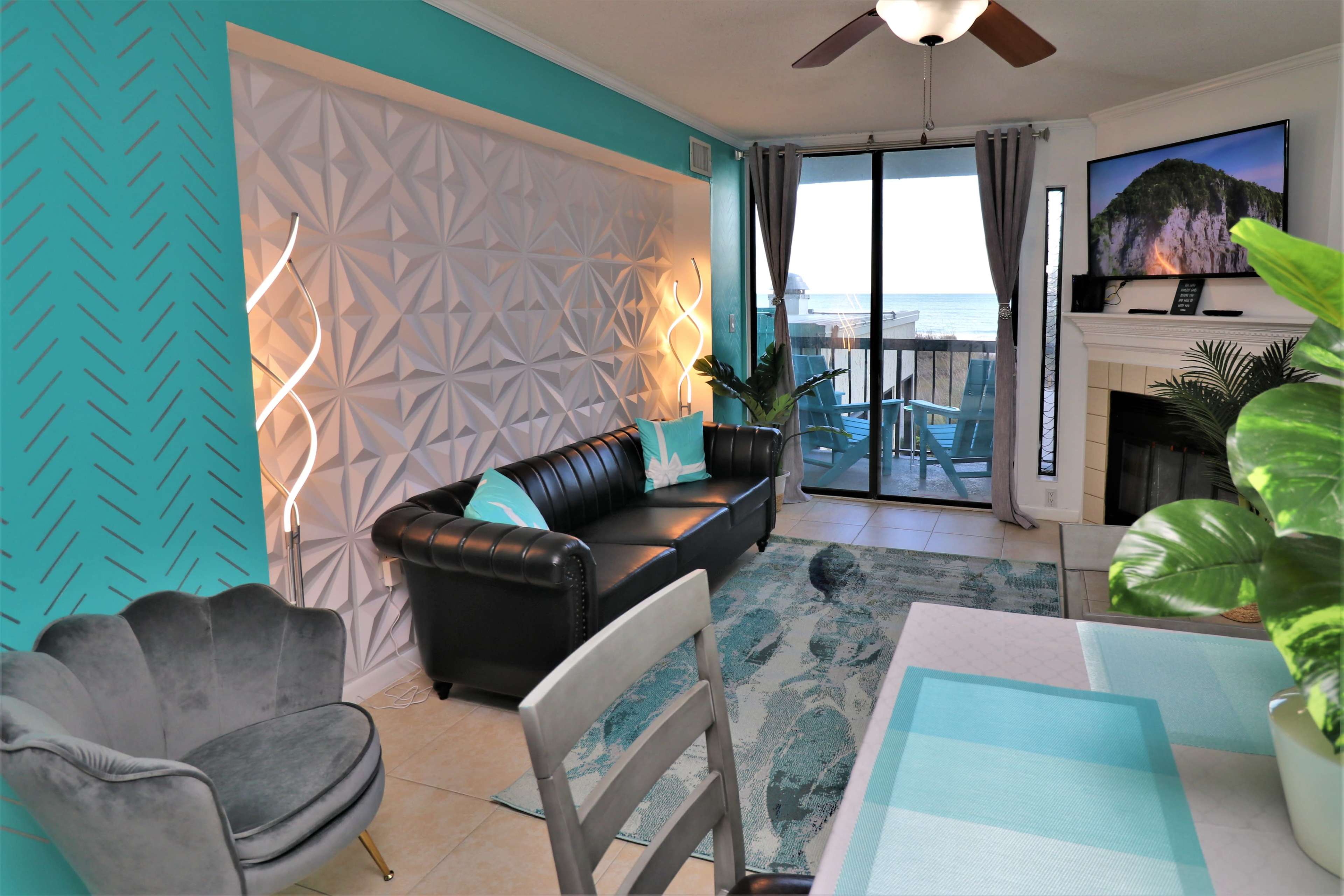 A modern living room with a black leather sofa, a patterned feature wall, and a large window overlooking the ocean.