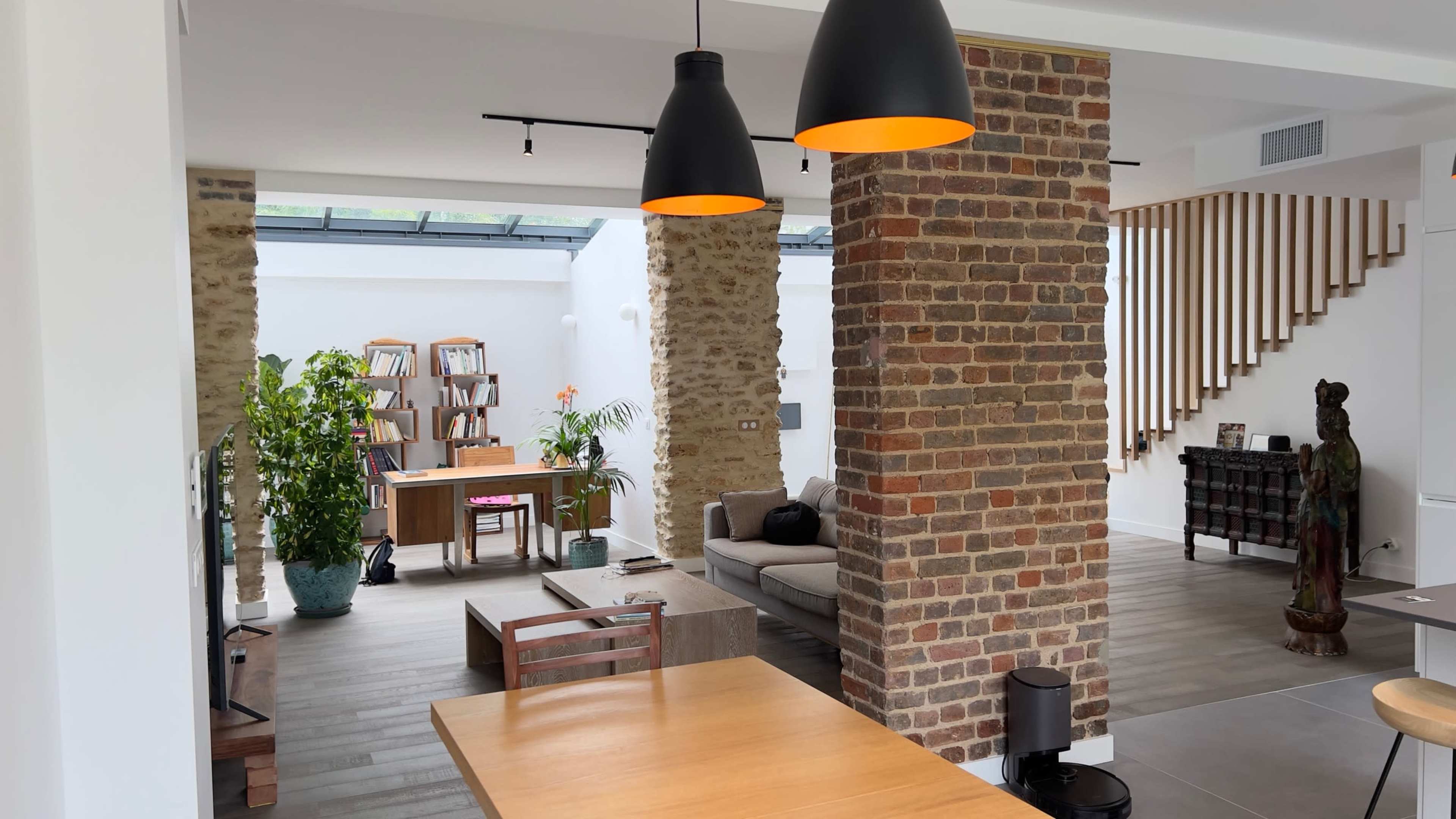 A modern living space featuring a combination of brick and neutral wall designs, with a sitting area, a staircase, and bookshelves visible in the background.