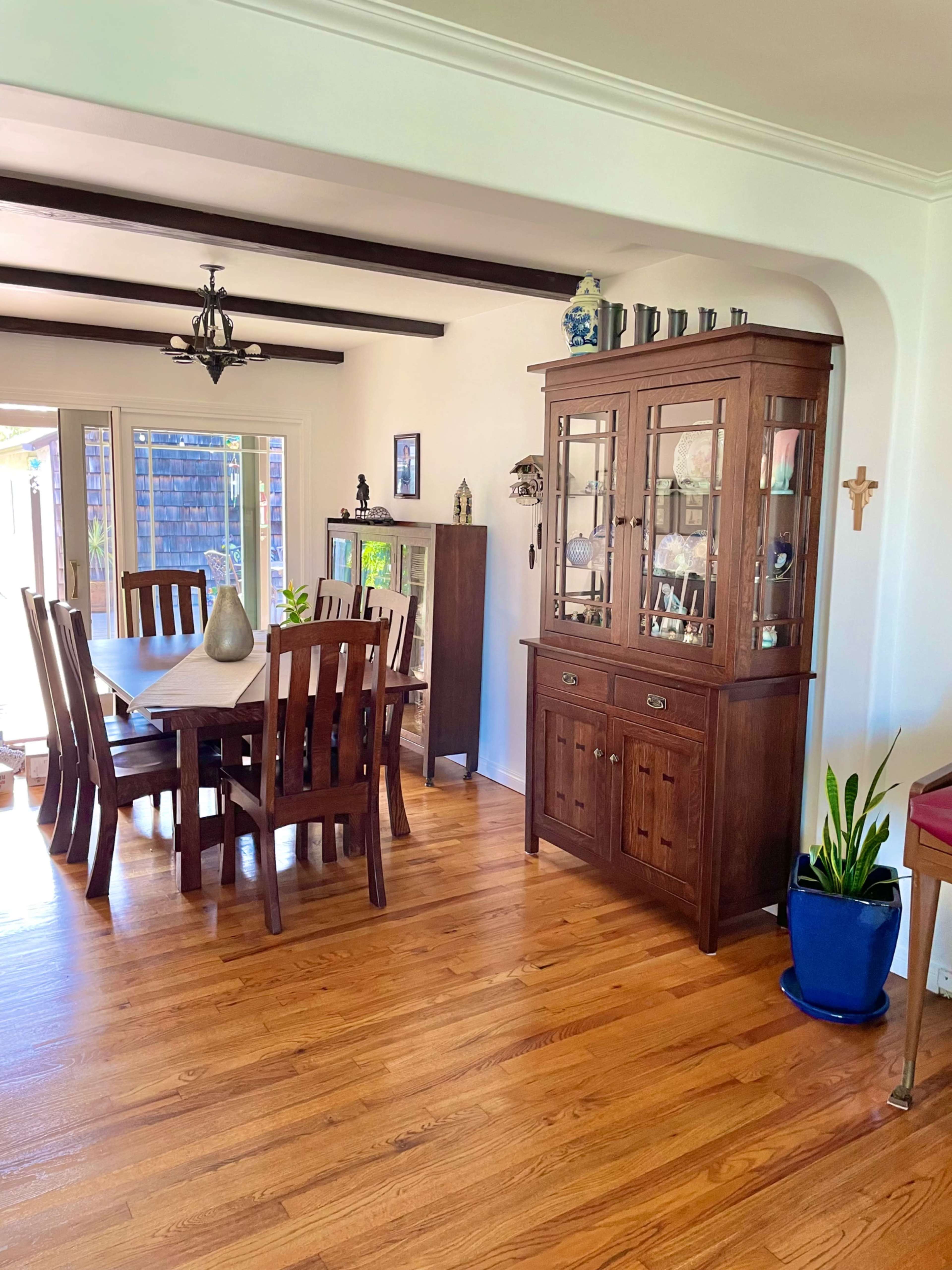 A dining room features a wooden table with chairs, a china cabinet, and hardwood flooring.
