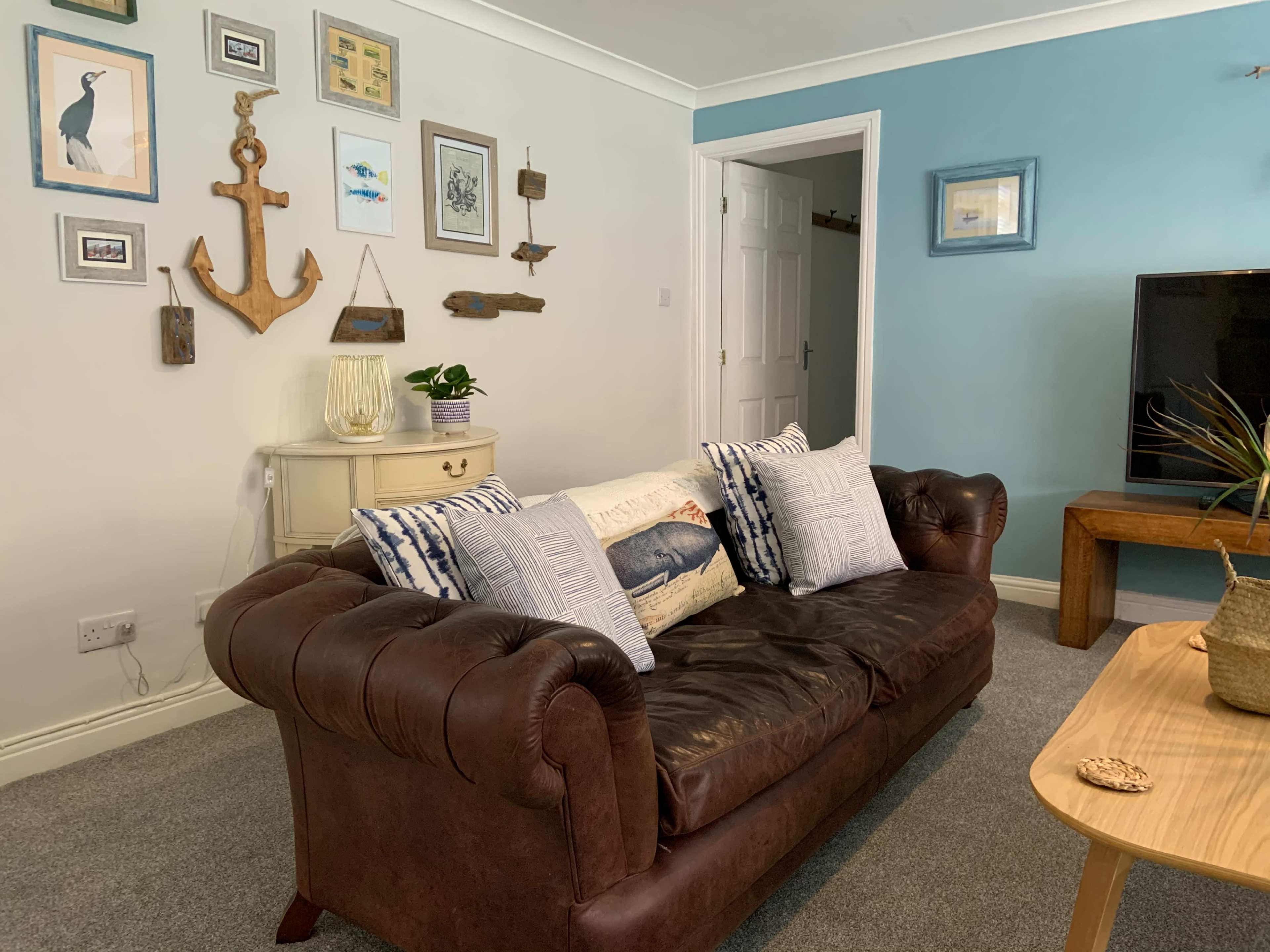 A living room with a brown leather couch, decorative pillows, a wooden coffee table, and various framed artworks on the wall.