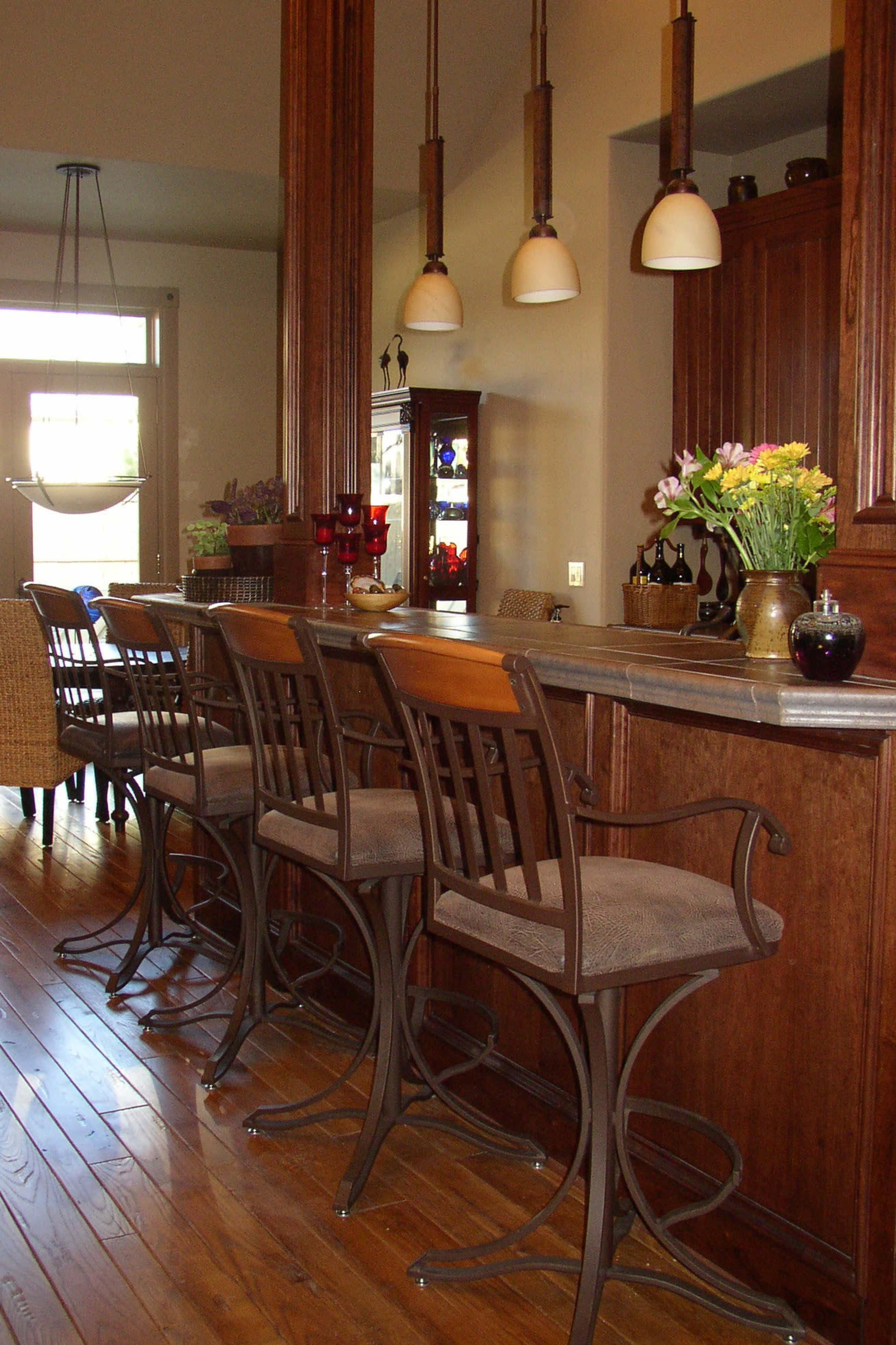 A kitchen bar area with several high-backed stools arranged in front of a counter, illuminated by hanging pendant lights.