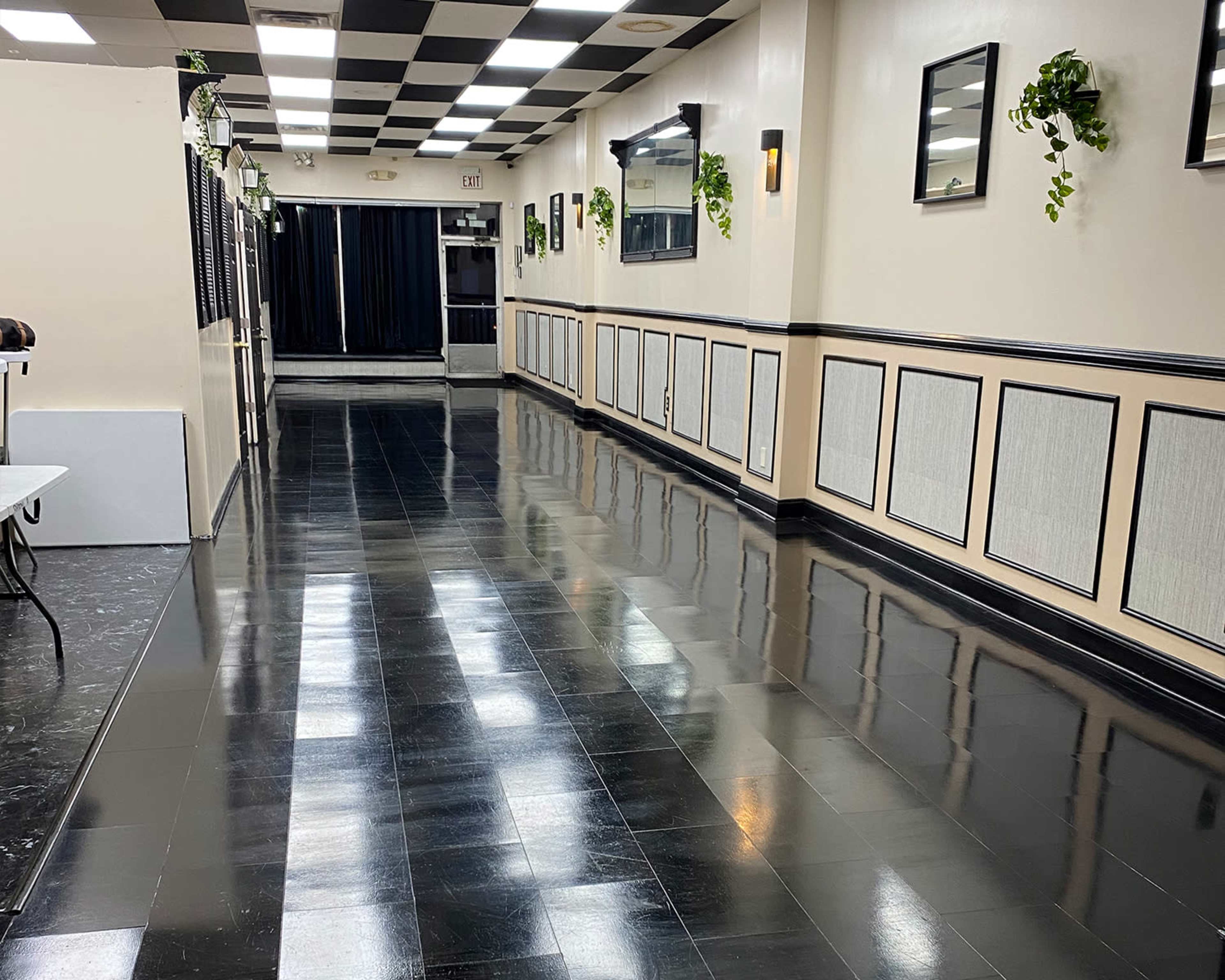 A narrow hallway with a checkerboard ceiling, polished black floors, and plants mounted on the walls.