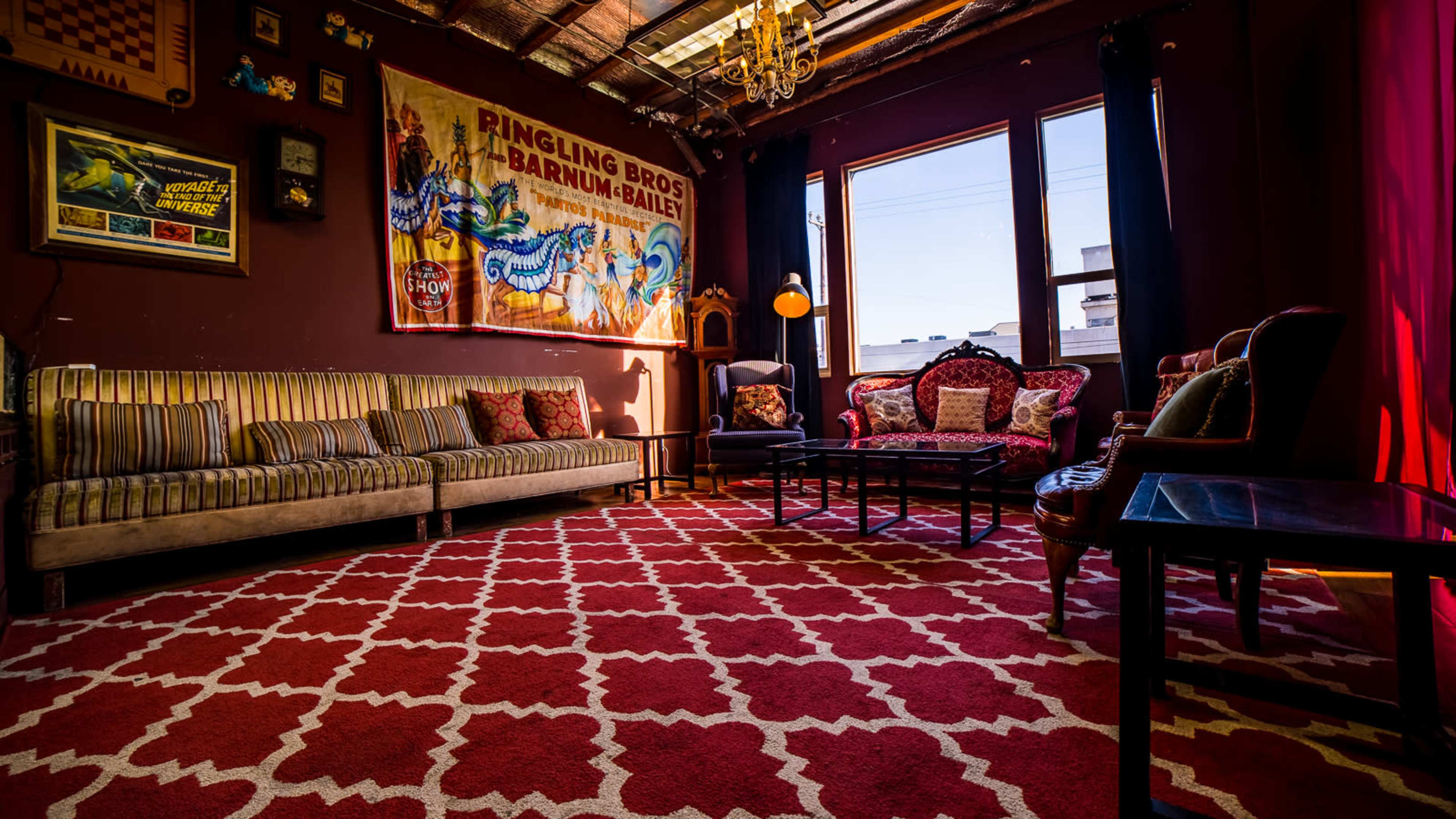 A cozy sitting area with patterned rugs, a vintage circus poster on the wall, and assorted furniture including a sofa, armchairs, and a coffee table.