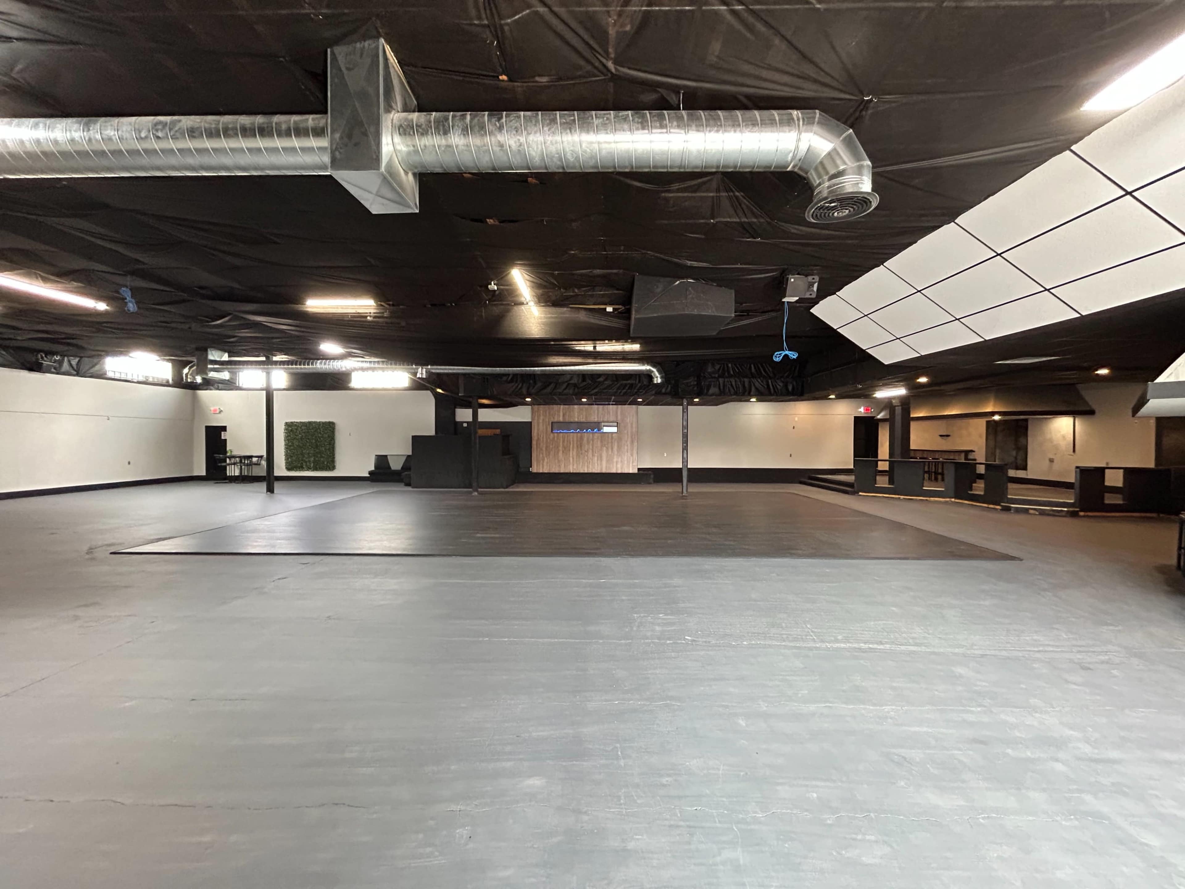 The image shows a spacious, empty interior of a commercial building with a black ceiling, gray flooring, and a wooden feature wall at the back.