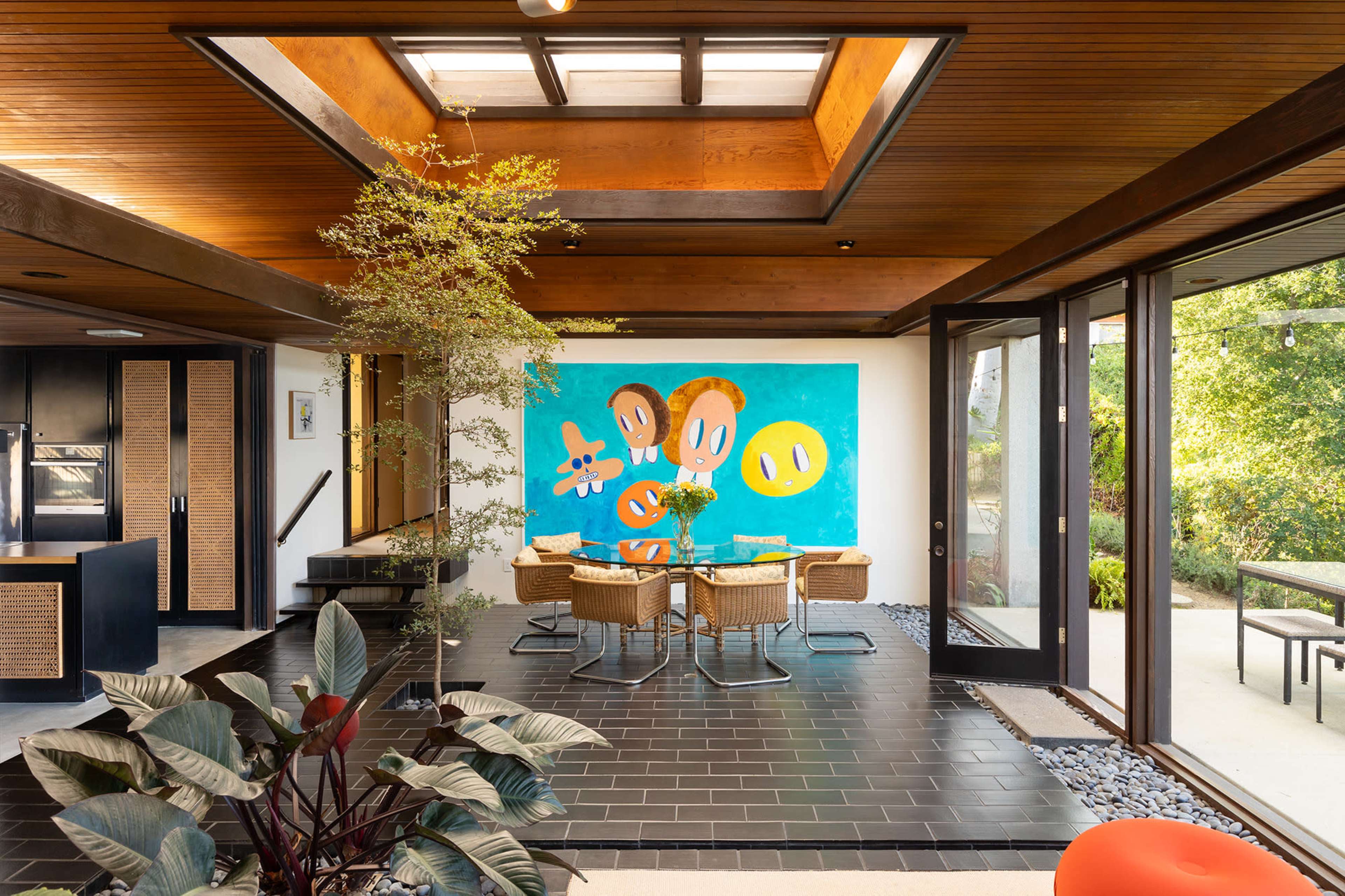 A modern dining area features a vibrant mural on one wall, surrounded by wicker chairs and a skylight overhead.
