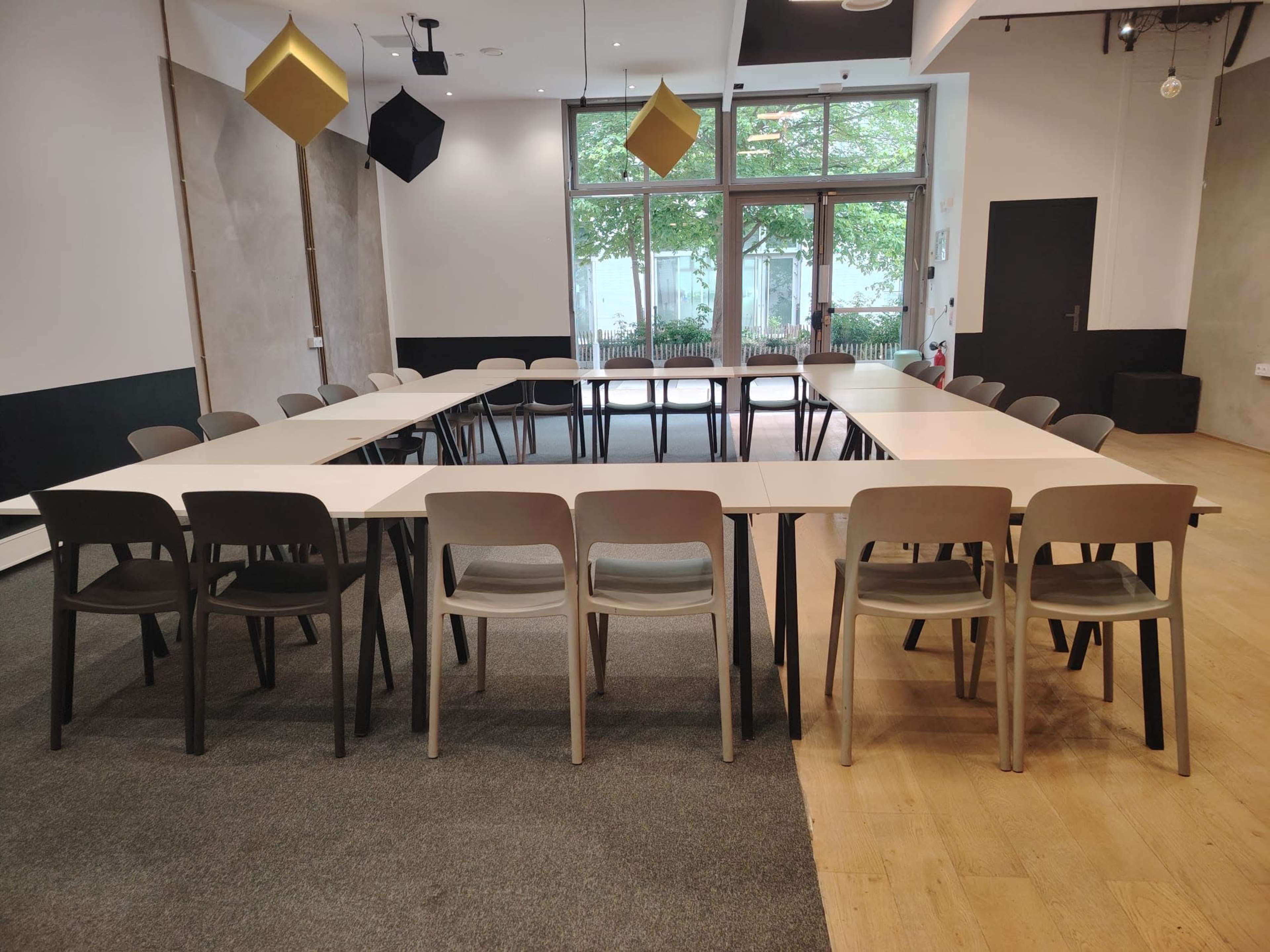 A rectangular conference room setup features a long table surrounded by chairs, with large windows and geometric hanging decorations.