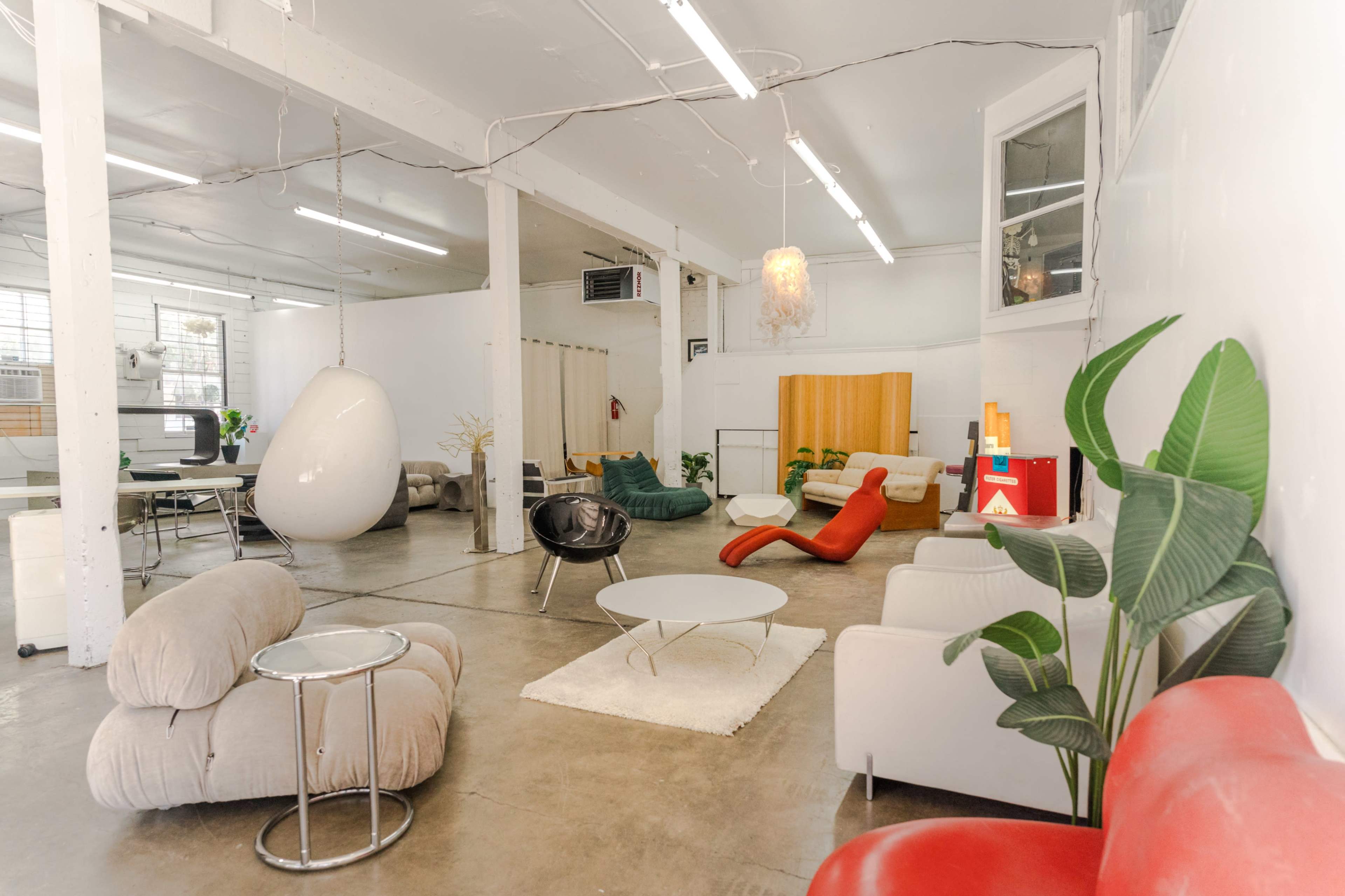 A spacious, modern interior with various seating areas, including a white hanging chair, contemporary sofas, and a round coffee table on a light rug.