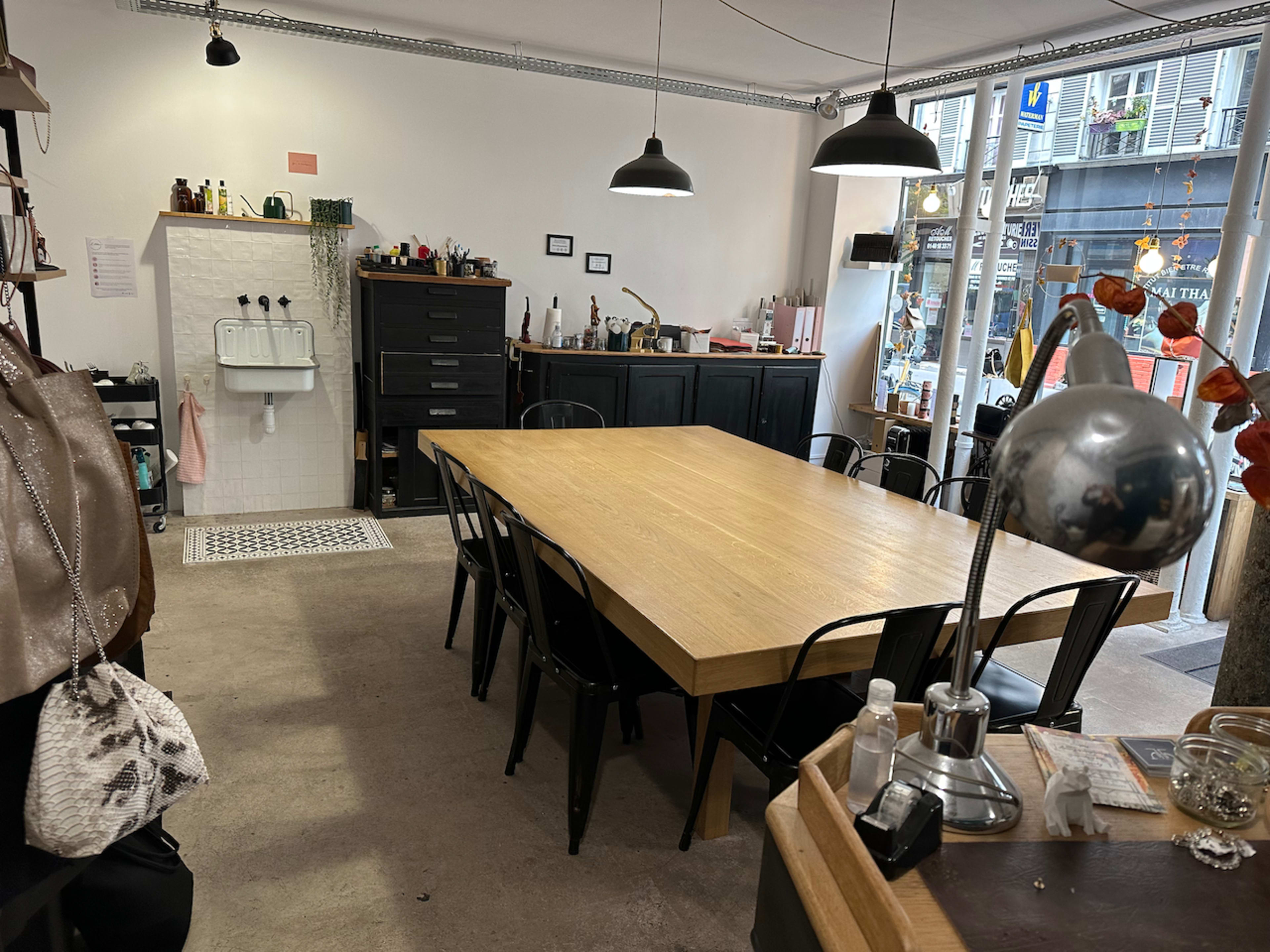 A spacious room features a large wooden table surrounded by black chairs, with a sink and storage cabinets against the wall.