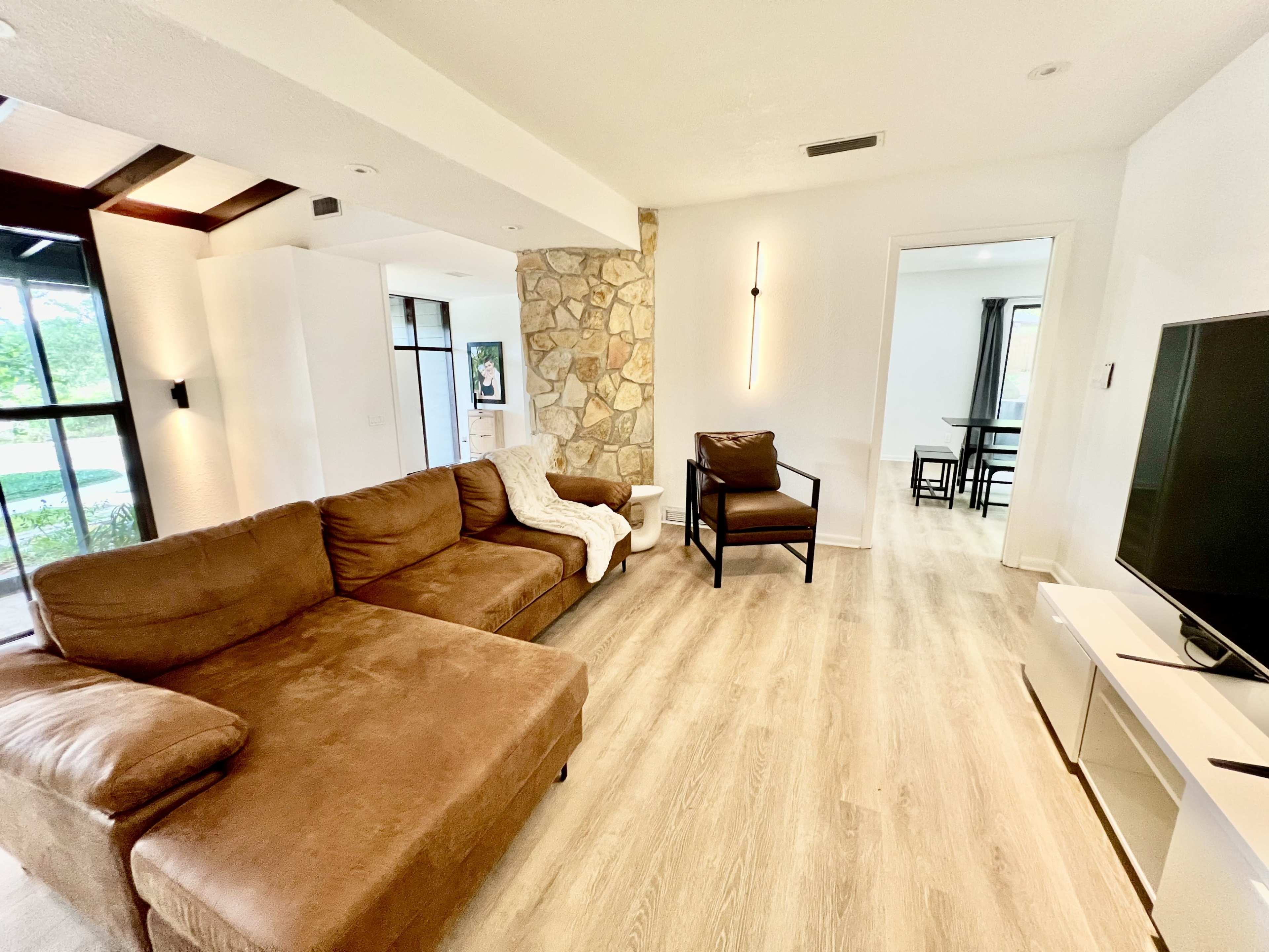 The image shows a living room with a brown sectional sofa, a stone accent wall, and a television on a white media console.