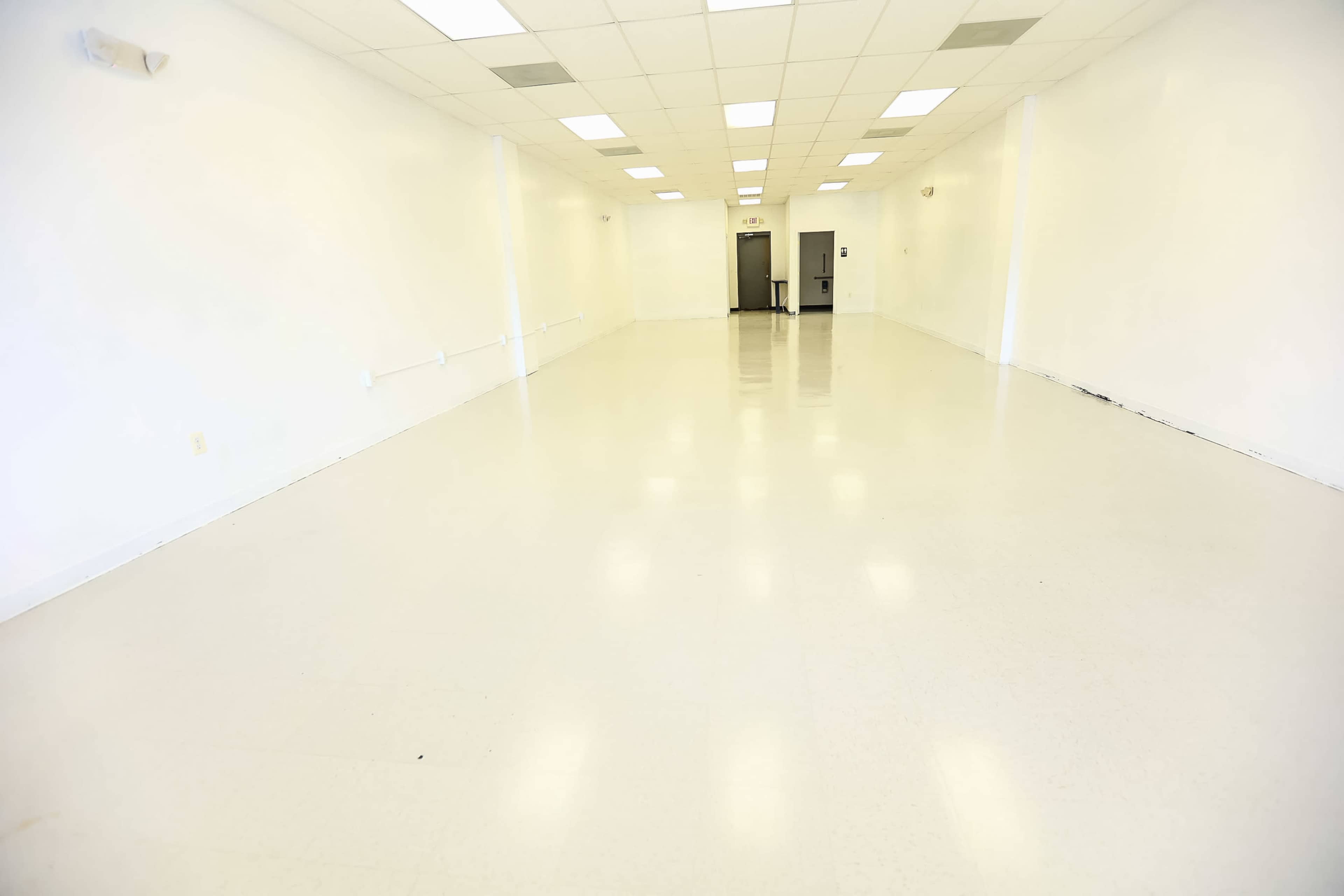 An empty, well-lit room with white walls and a smooth, shiny floor.