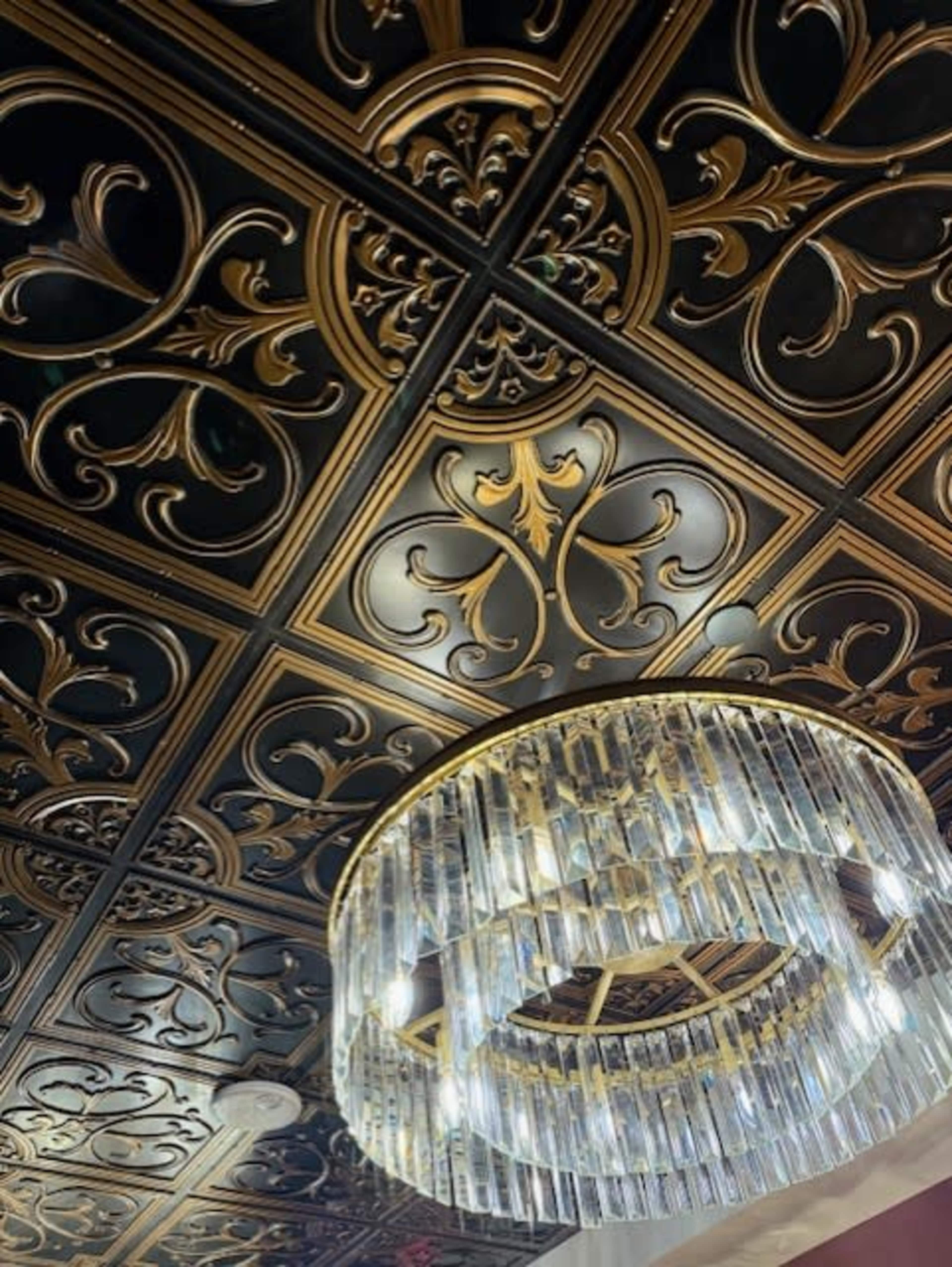 The image shows a ceiling with ornate black and gold patterns topped by a circular crystal chandelier.