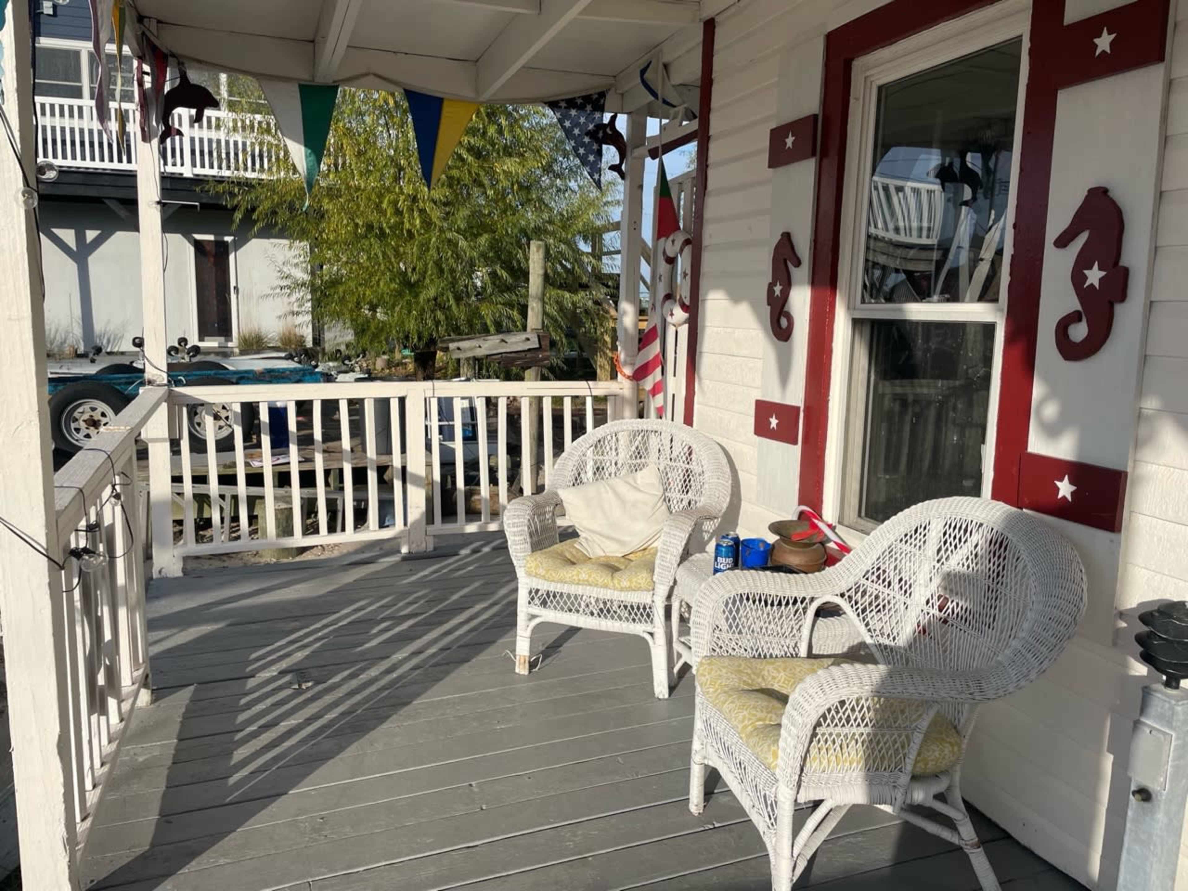 A covered porch with two wicker chairs and a small table, adorned with decorative seahorse designs and colorful bunting overhead.