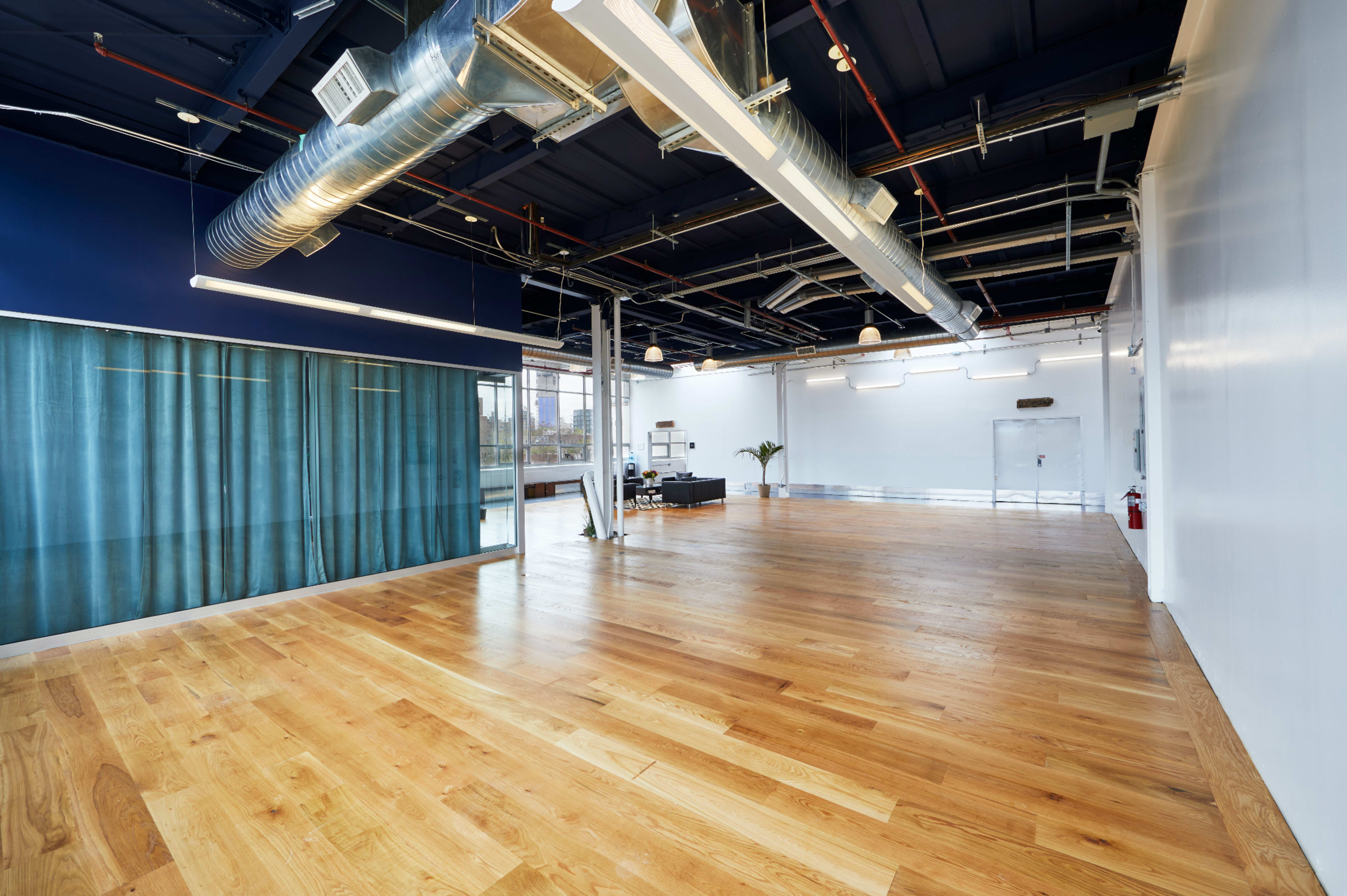 The image shows a spacious, modern interior with wooden flooring, large windows, and a blue wall with curtains.