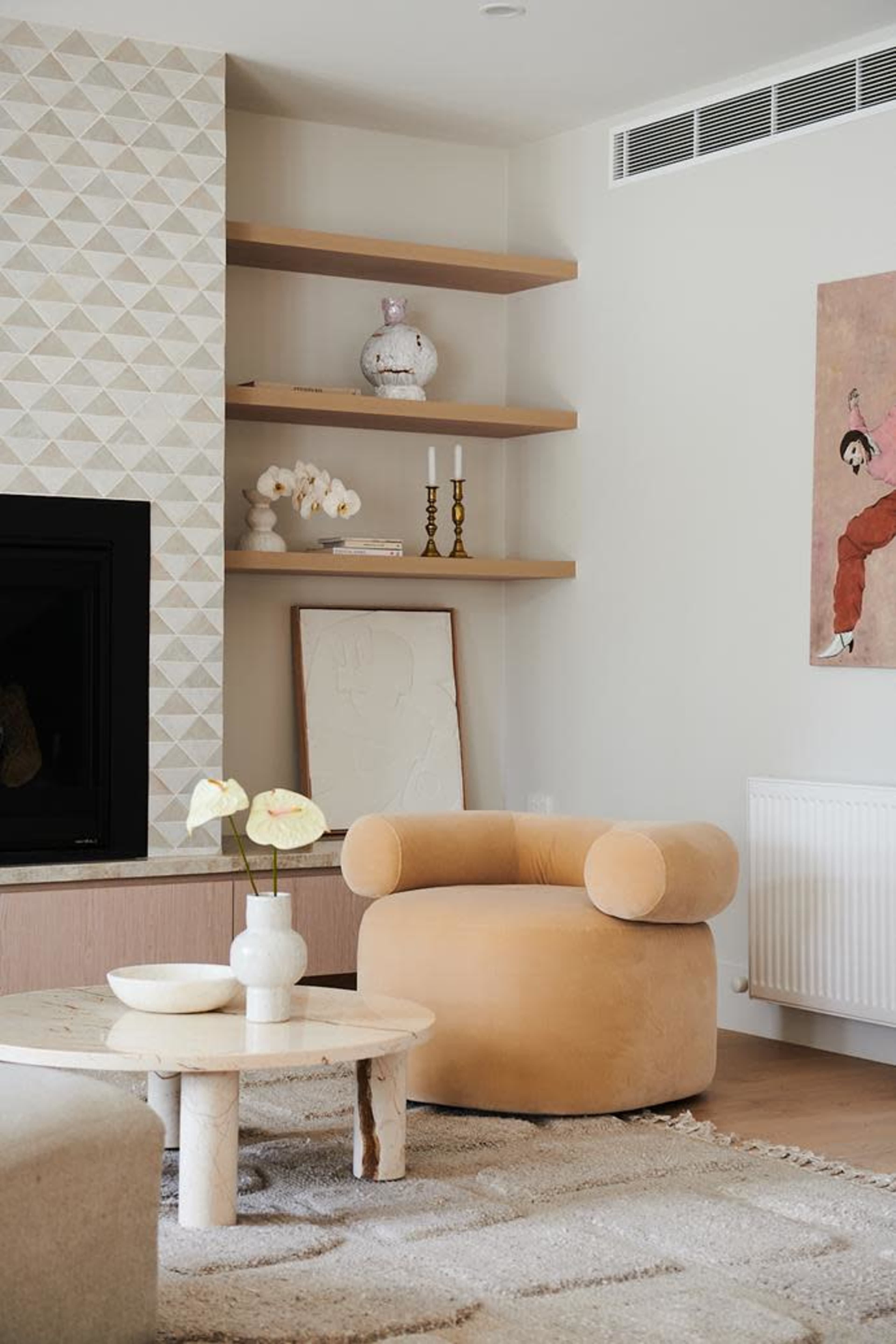 A cozy living room features a circular tan chair beside a round coffee table, with a textured wall and open shelving in the background.