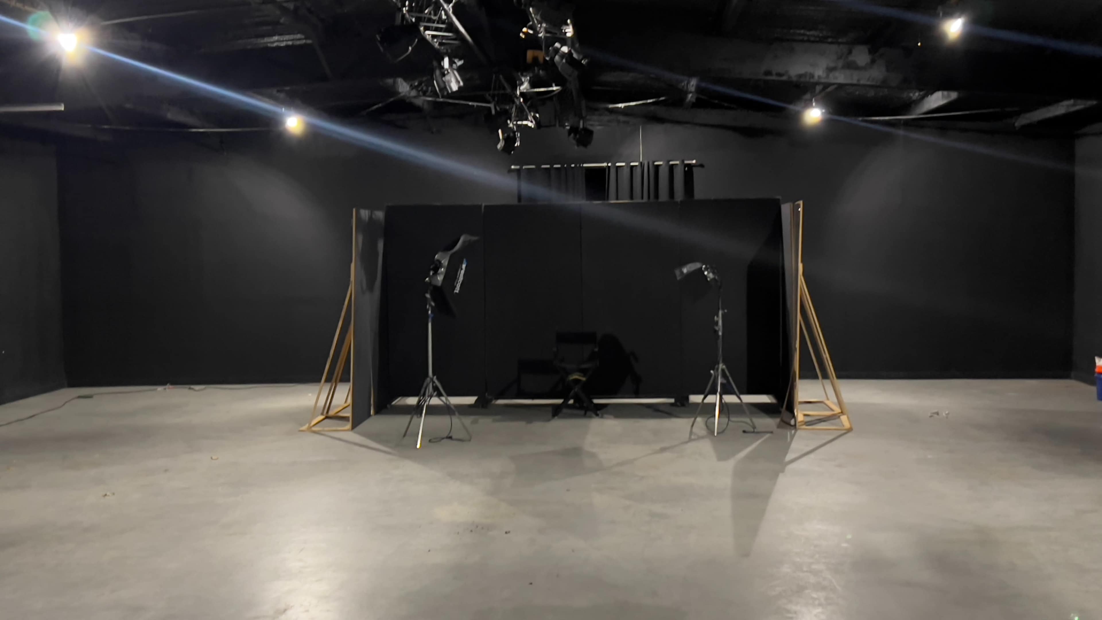 An empty studio space with a black backdrop, two lighting stands, and a chair positioned in front of the backdrop.