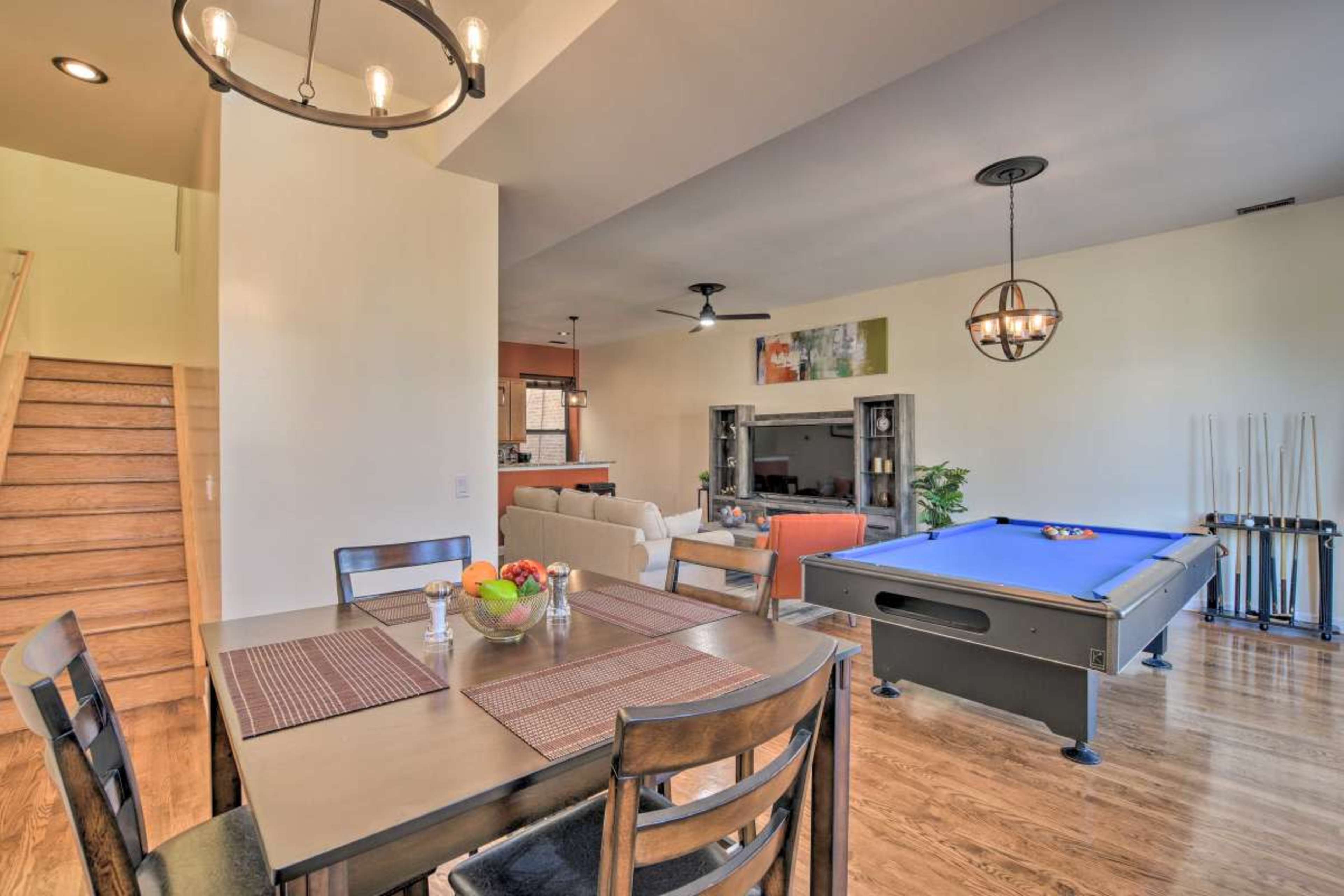 A modern interior featuring a dining table with fruit, a pool table, and a staircase leading to an upper level.
