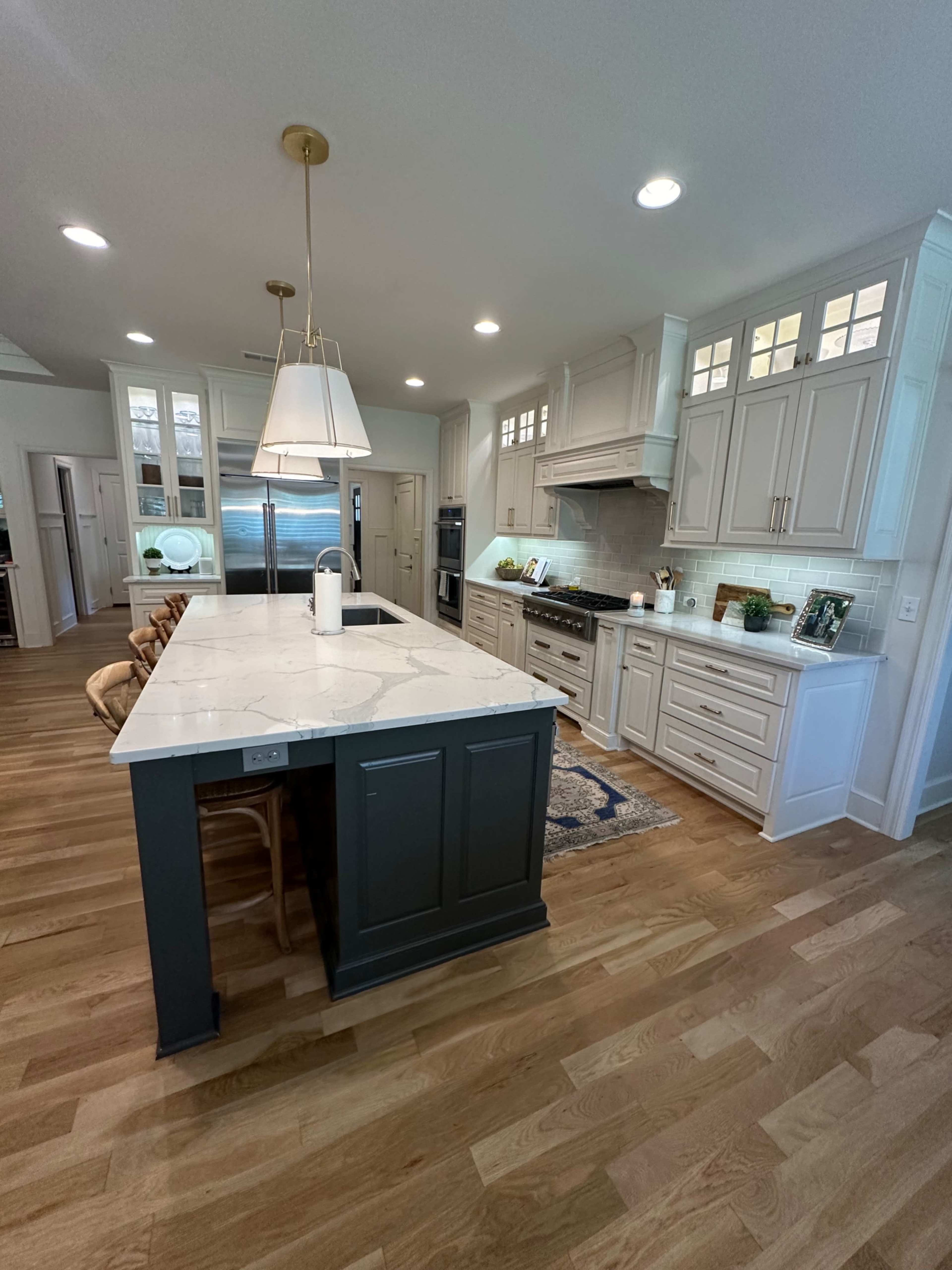 A modern kitchen featuring a large island with a white countertop, light cabinetry, and wooden flooring.