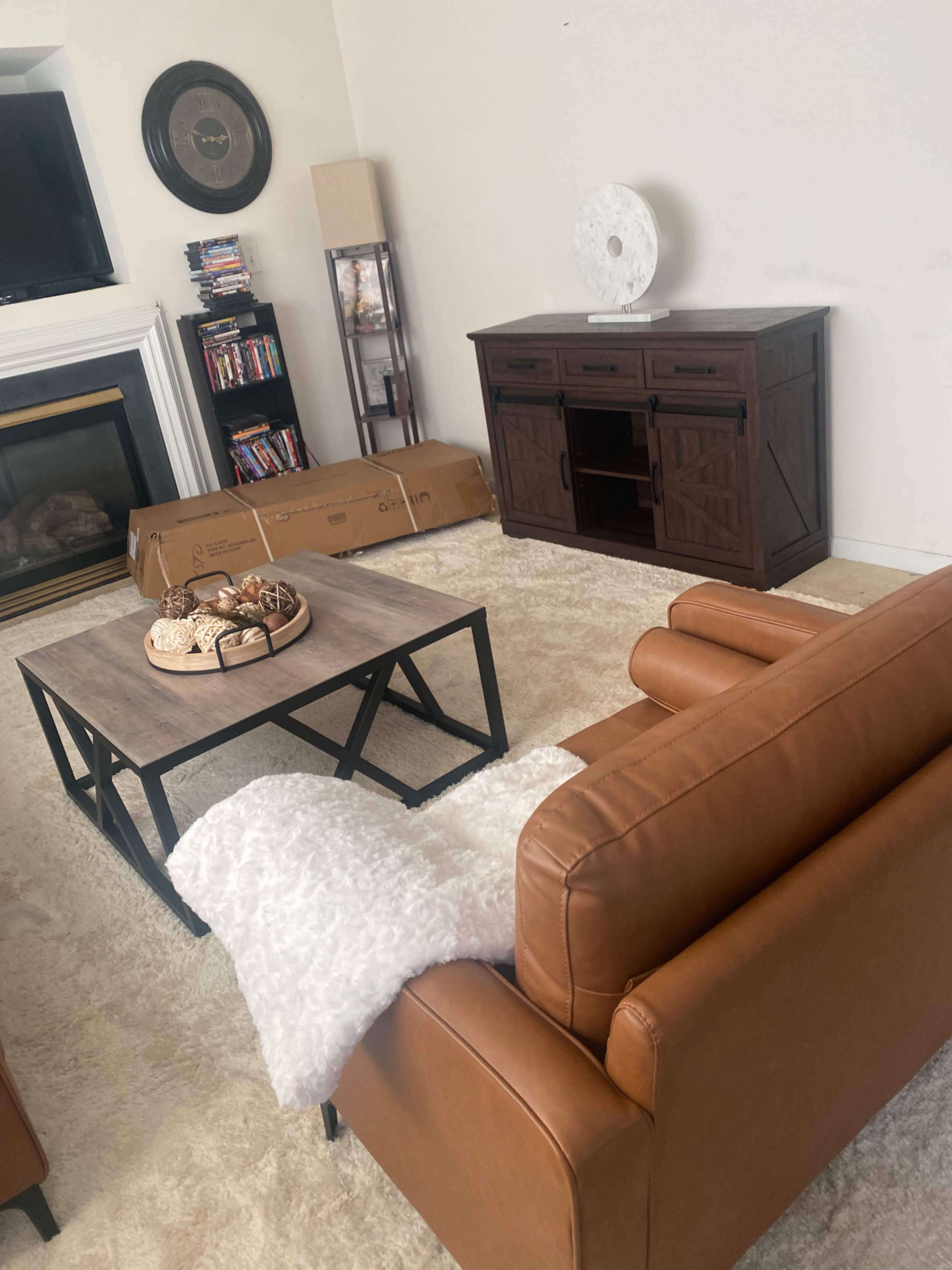 The image depicts a living room featuring a brown leather sofa, a coffee table with a decorative tray, a wooden TV console, and a fireplace in the background.