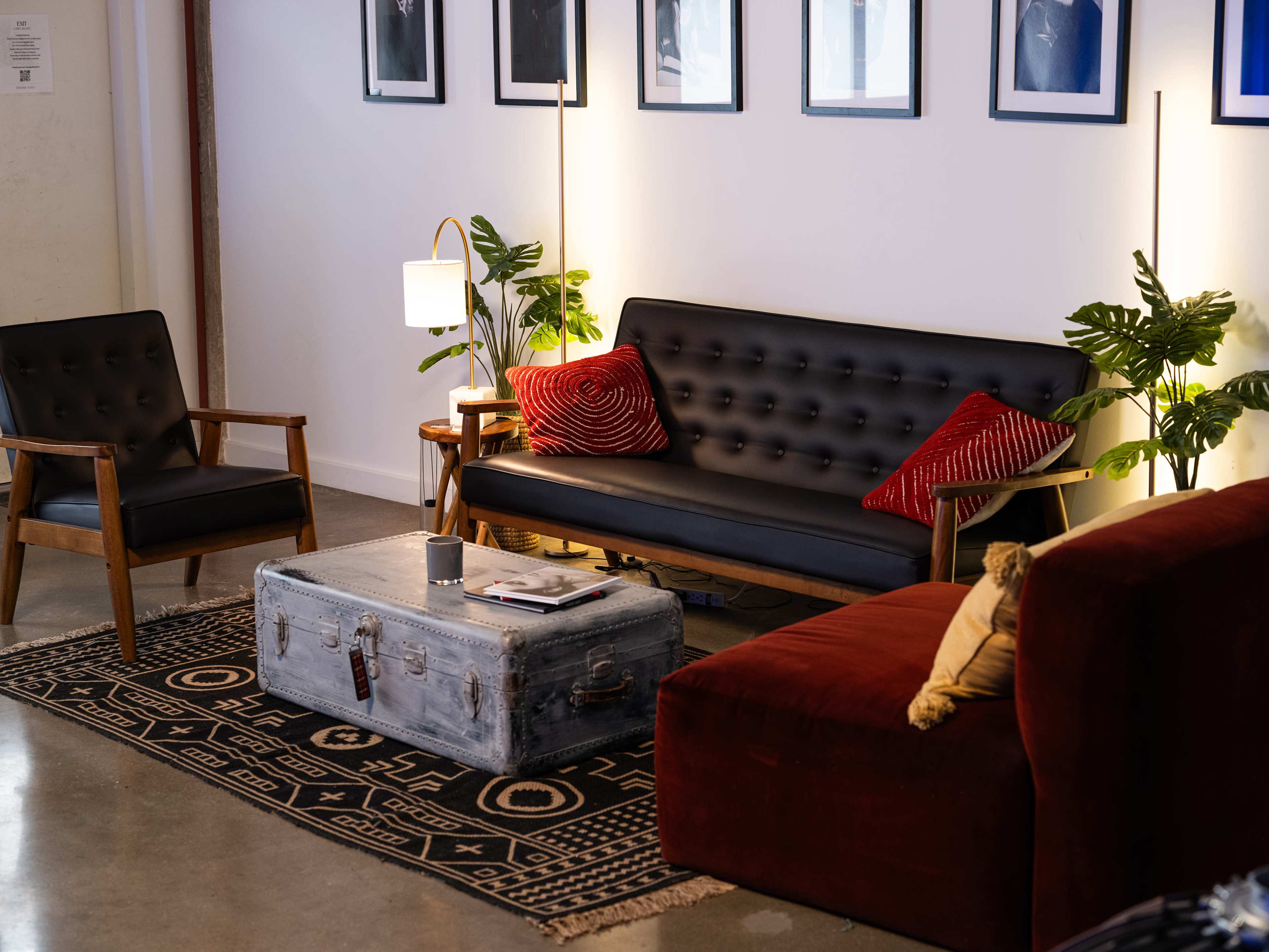The scene features a cozy living area with a black tufted sofa, a red armchair, a vintage trunk coffee table, and framed pictures on the wall.