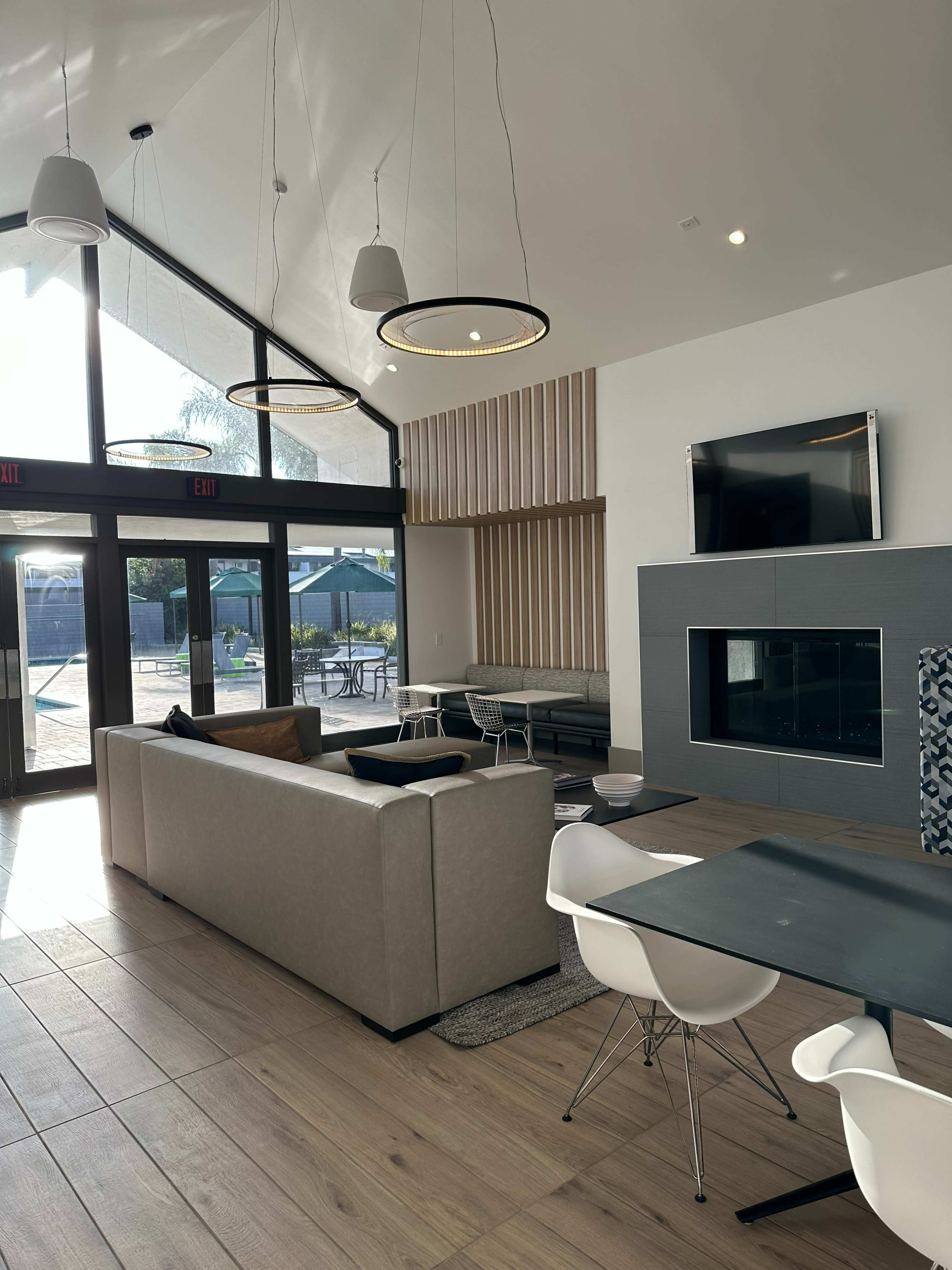 A modern lounge area with a tall ceiling, a sofa, a dining table, and a large window overlooking an outdoor space.