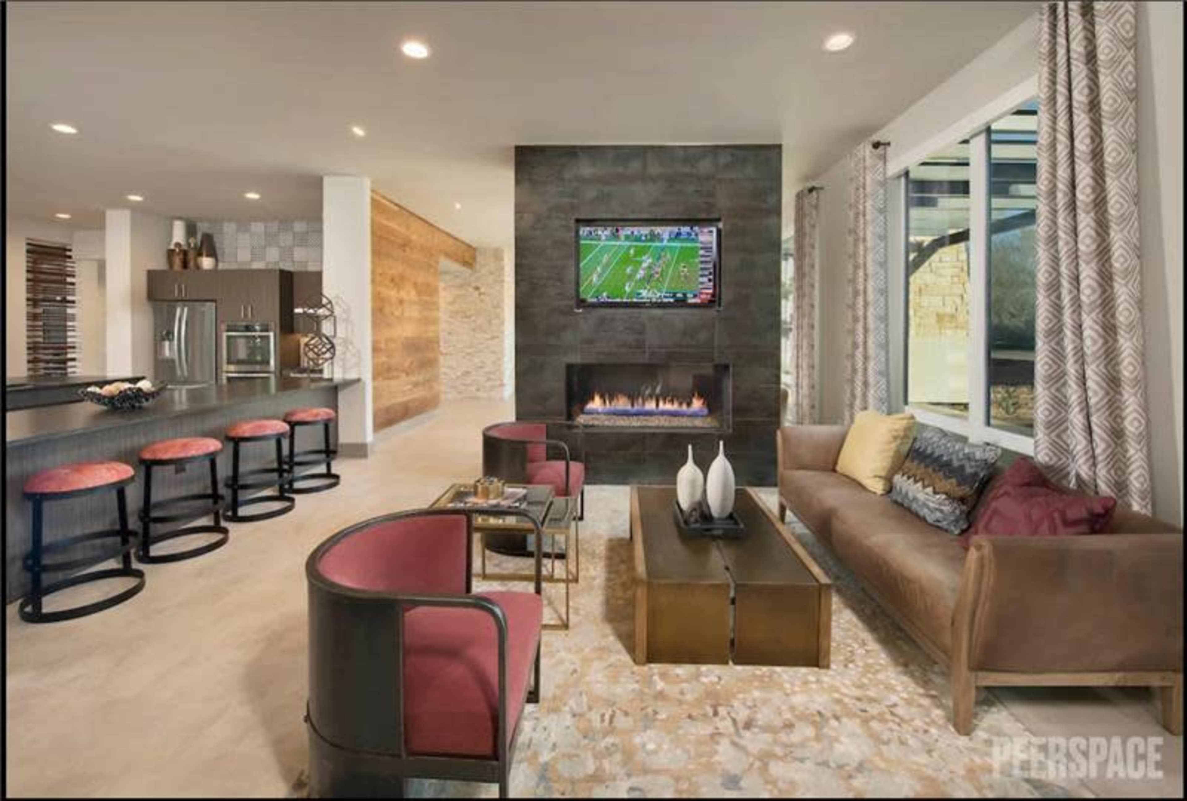 The image shows a modern living room with large windows, a fireplace, and a television mounted on the wall above a sleek coffee table.