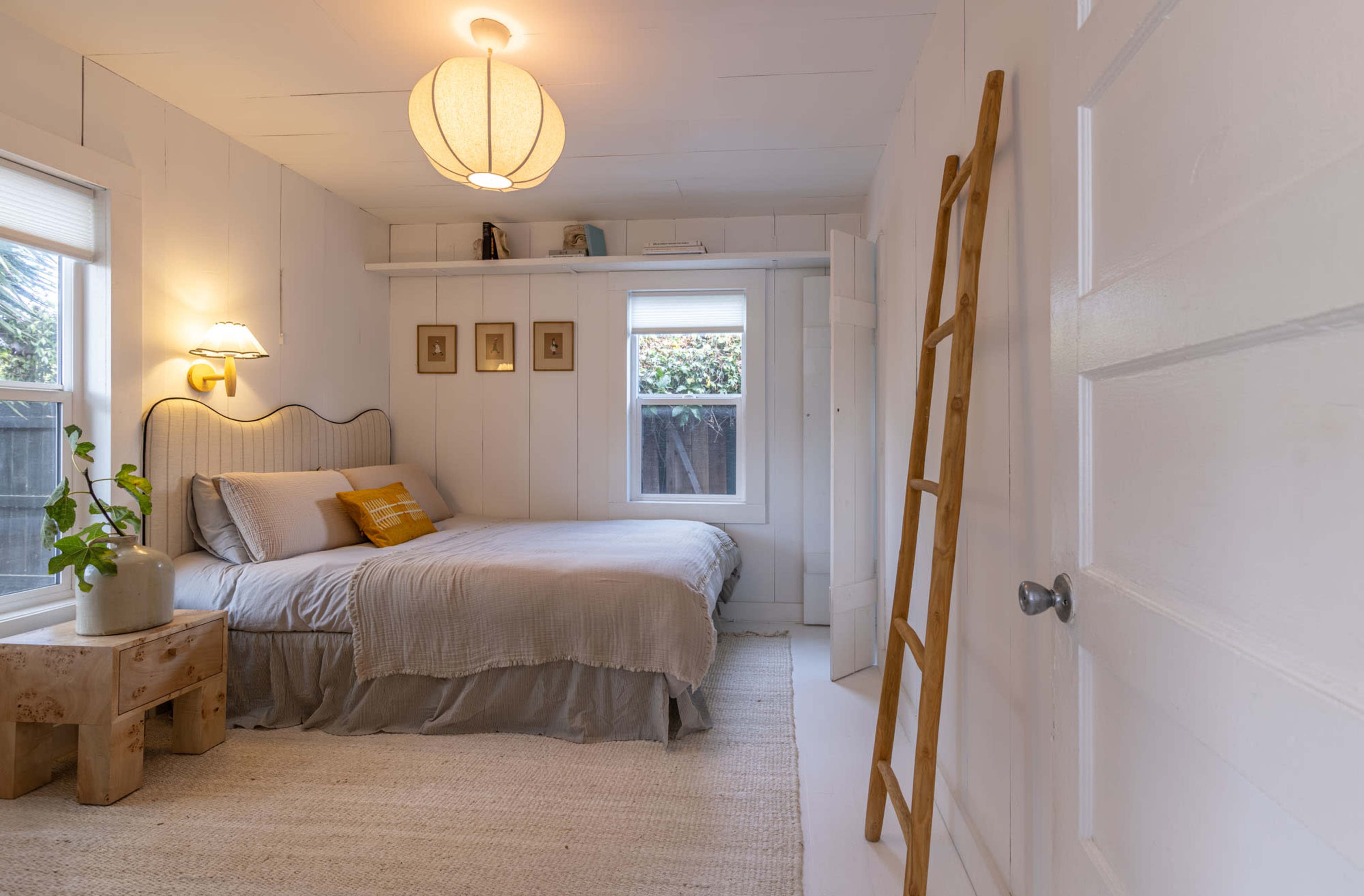 The image shows a cozy bedroom with a bed, a wooden ladder against the wall, and natural light coming through a window.