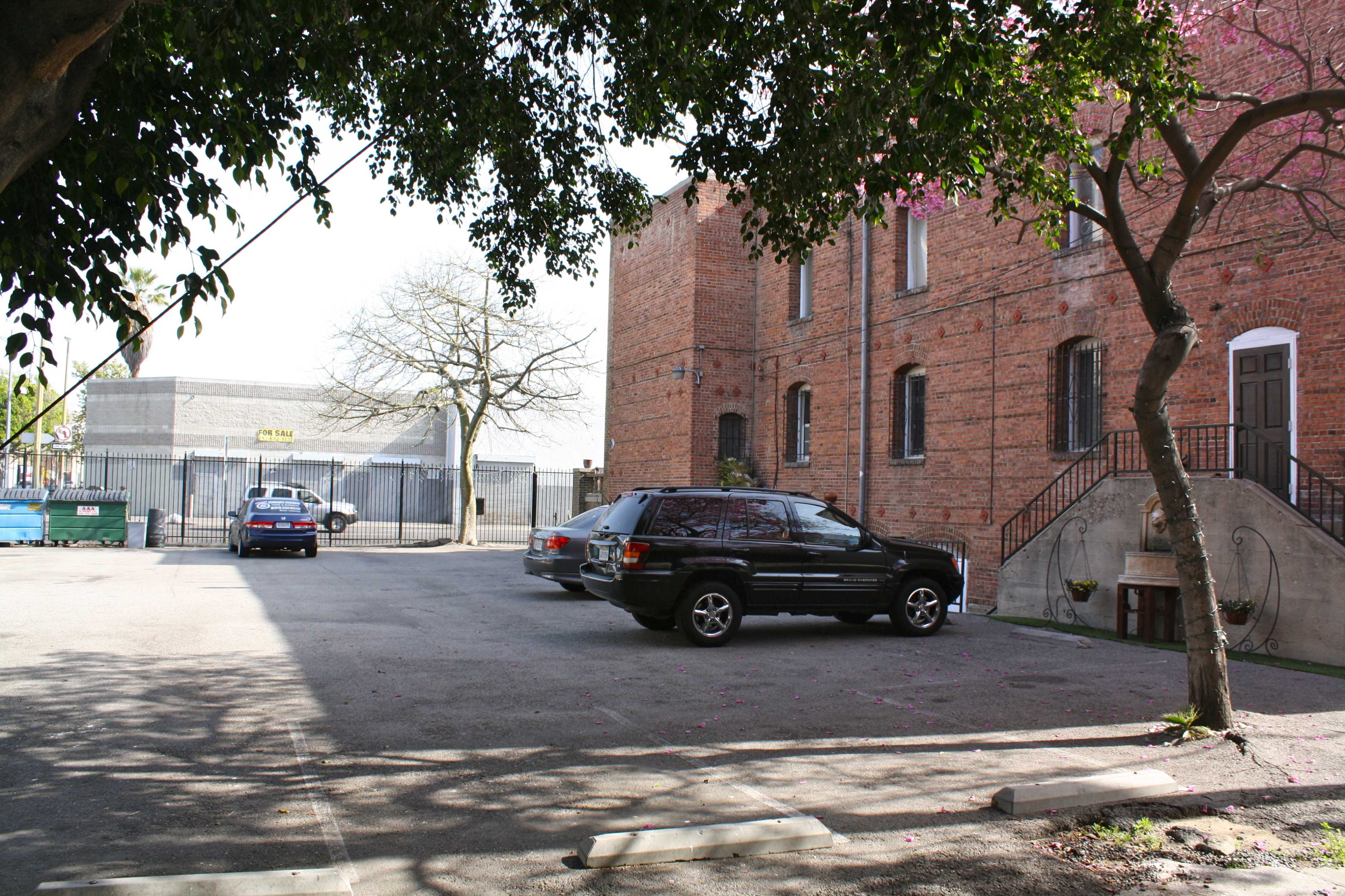 A secluded parking area with two parked vehicles beside a brick building and a tree overhead.