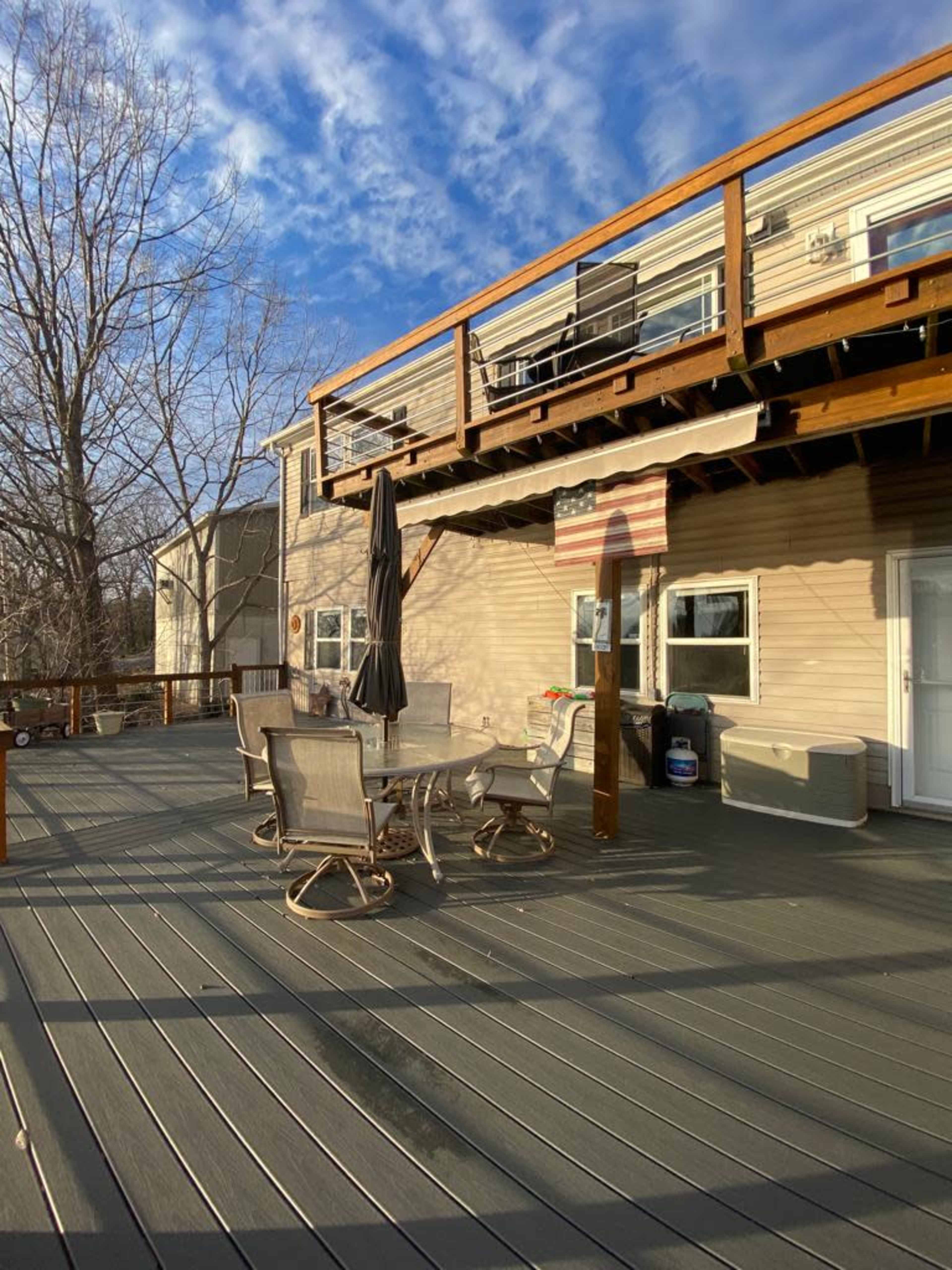 A spacious wooden deck features a table and chairs set, an umbrella, and a view of a two-story house with a flag display.