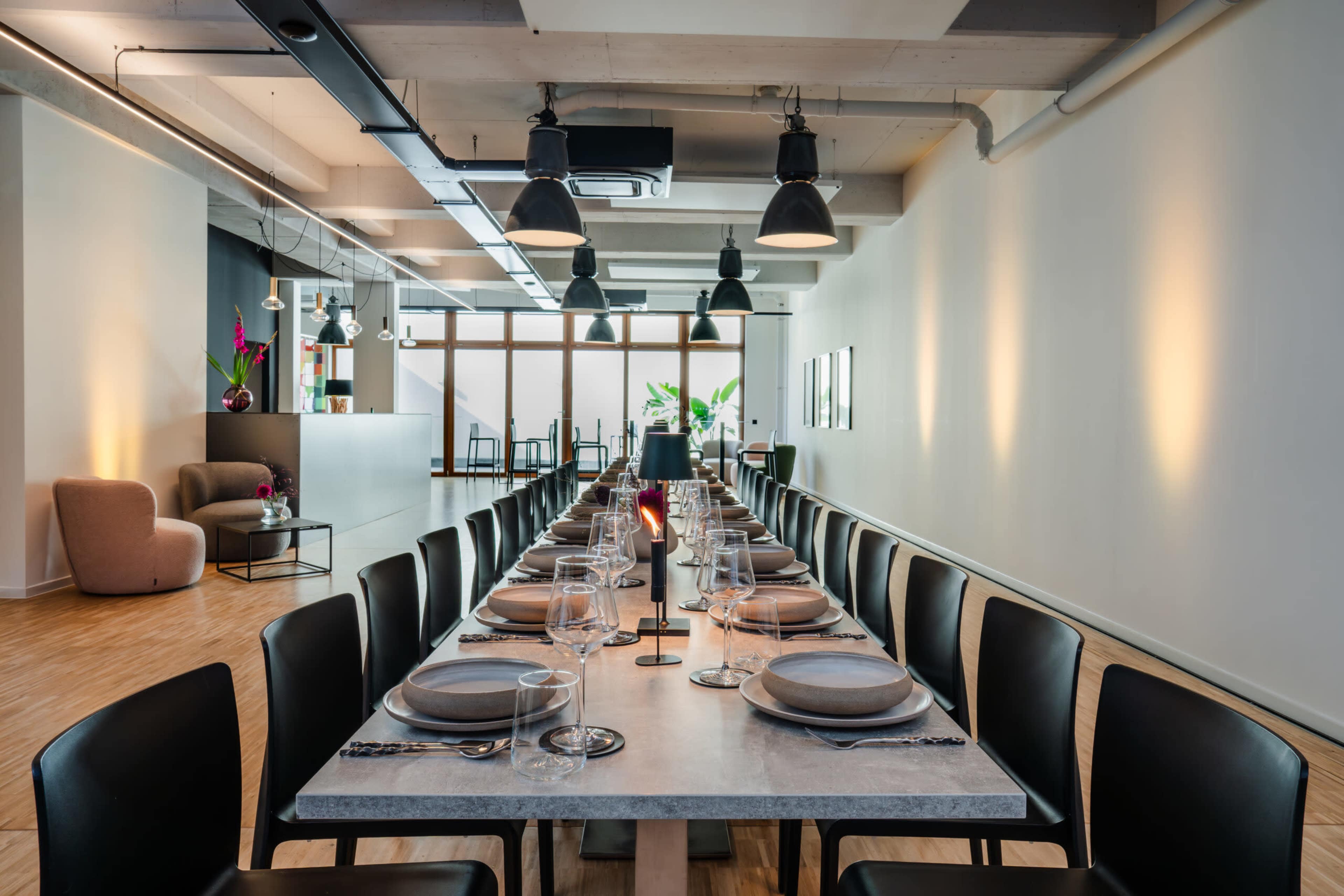 A long dining table is set with plates and glasses in a modern, well-lit restaurant space.