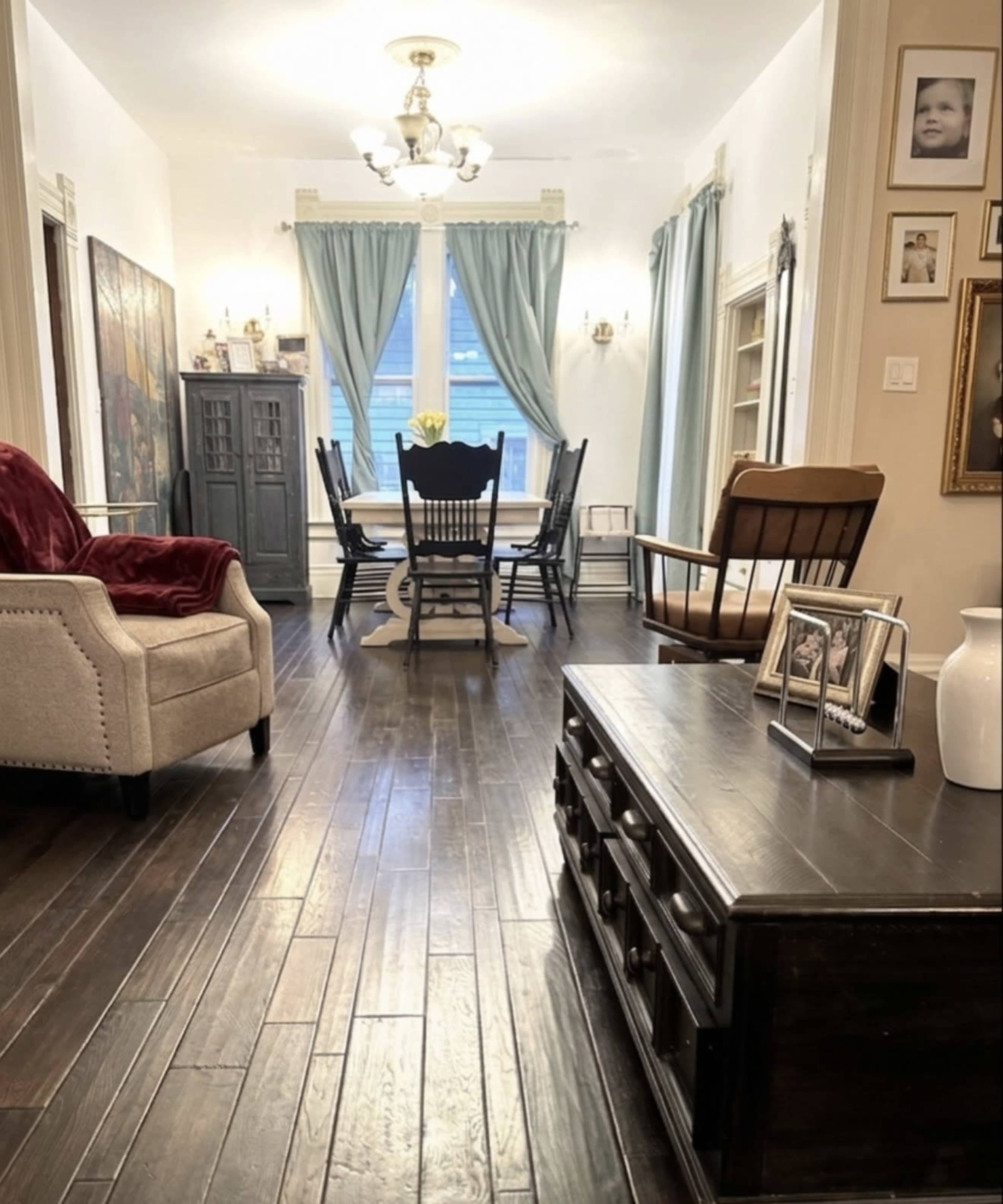 The image shows a dining area with a wooden table and chairs, a comfortable armchair, and decorative items on the walls and furniture.