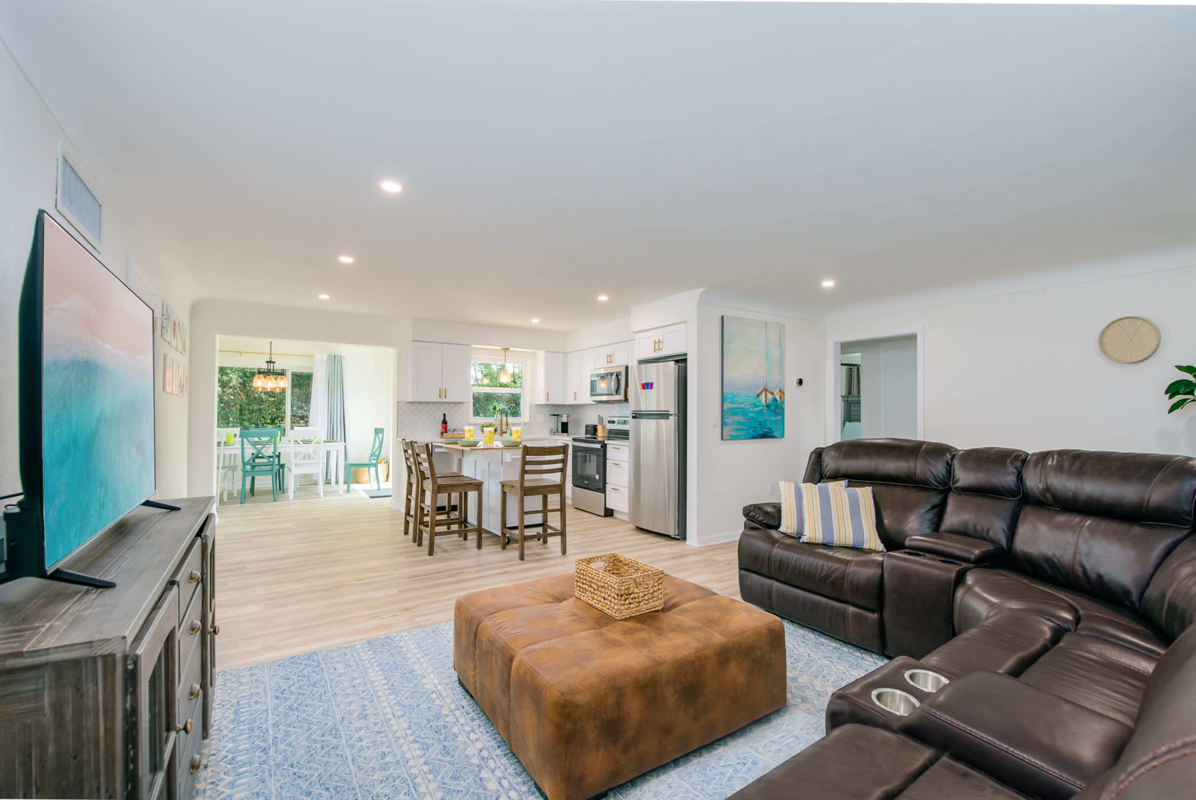 A modern living room features a sectional couch, a coffee table, and an open kitchen area with dining space and access to an outdoor patio.