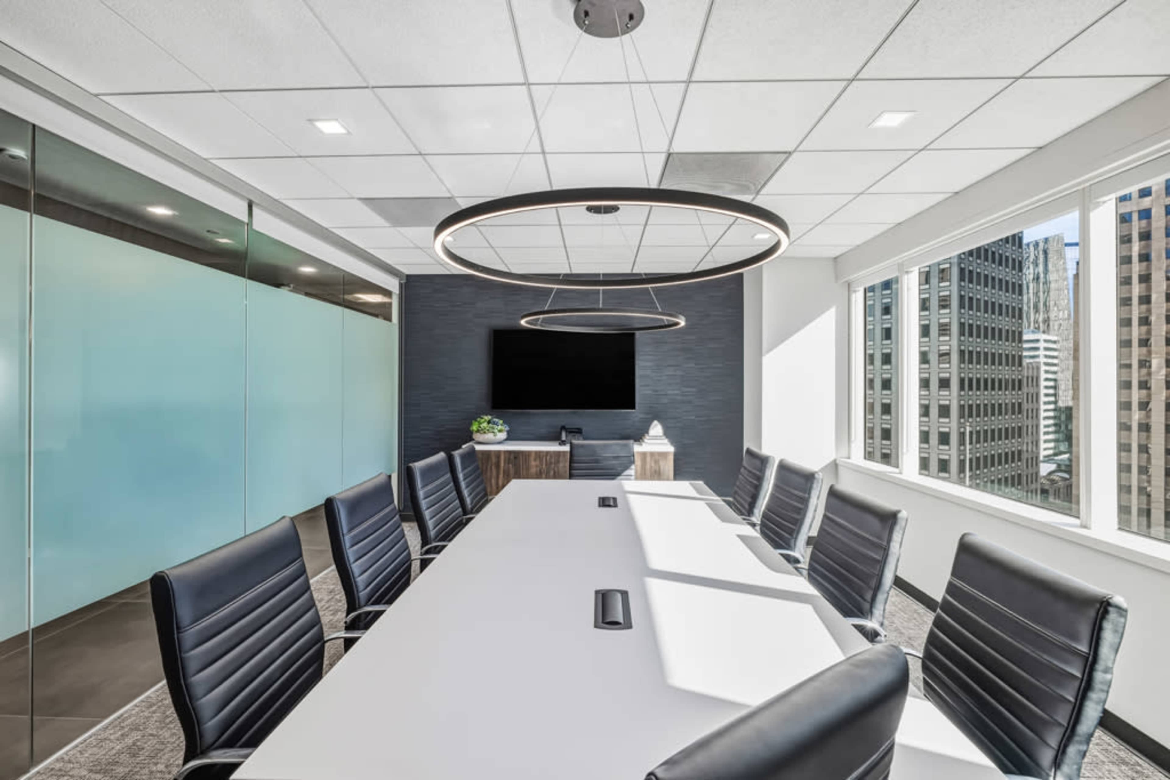 The image shows a modern conference room with a long white table, black leather chairs, and large windows overlooking a cityscape.