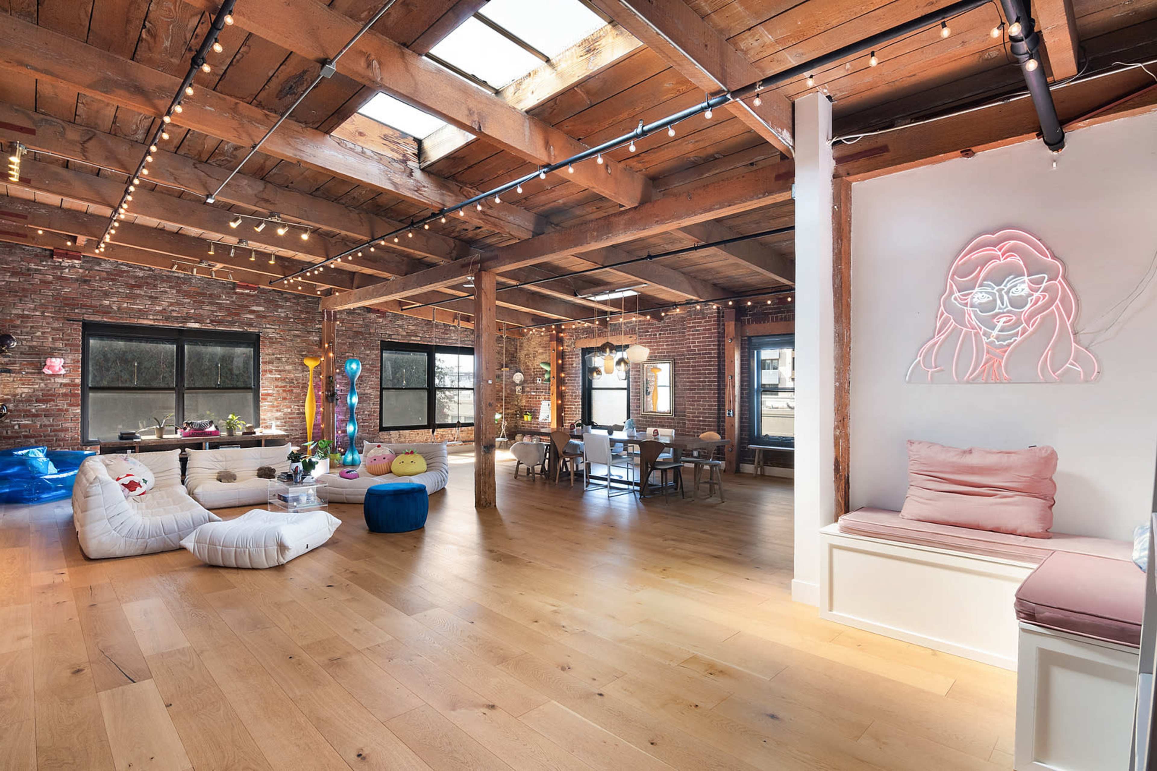 A spacious loft with exposed brick walls, wooden beams, and large windows, featuring a mix of seating areas and decorative elements.