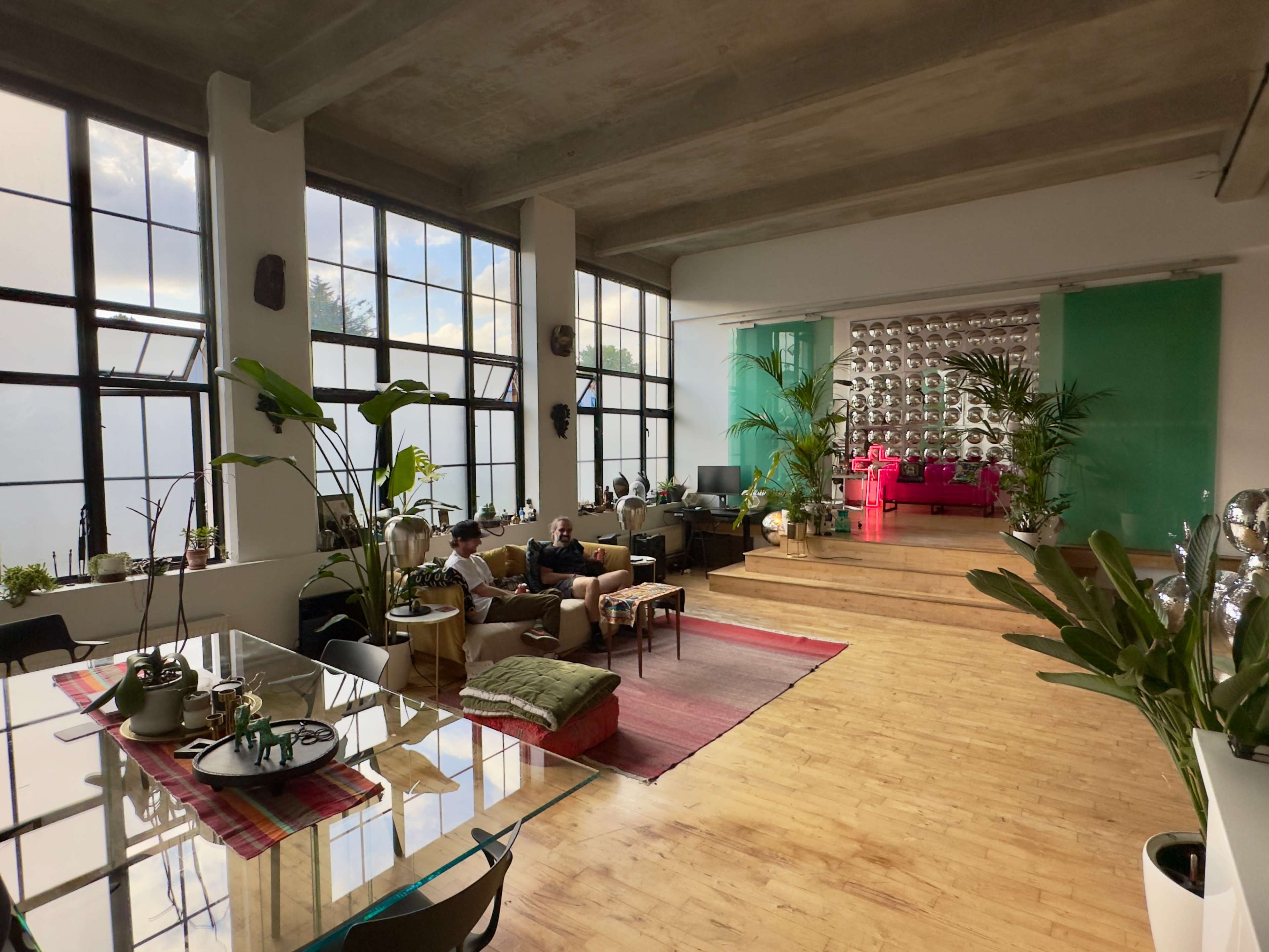 The image depicts a modern open-concept living space with large windows, a glass dining table, and colorful furniture, including a pink couch.