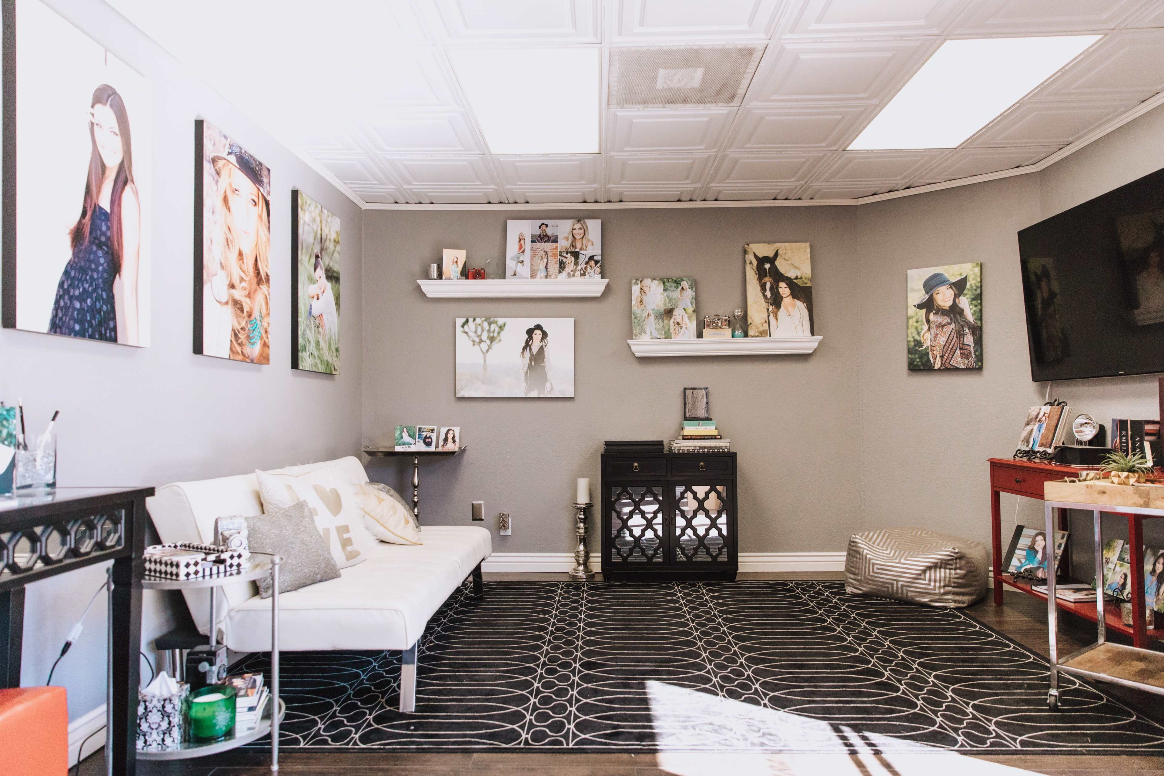 A cozy living room with a white sofa, a dark patterned rug, and various framed photographs on the gray walls.