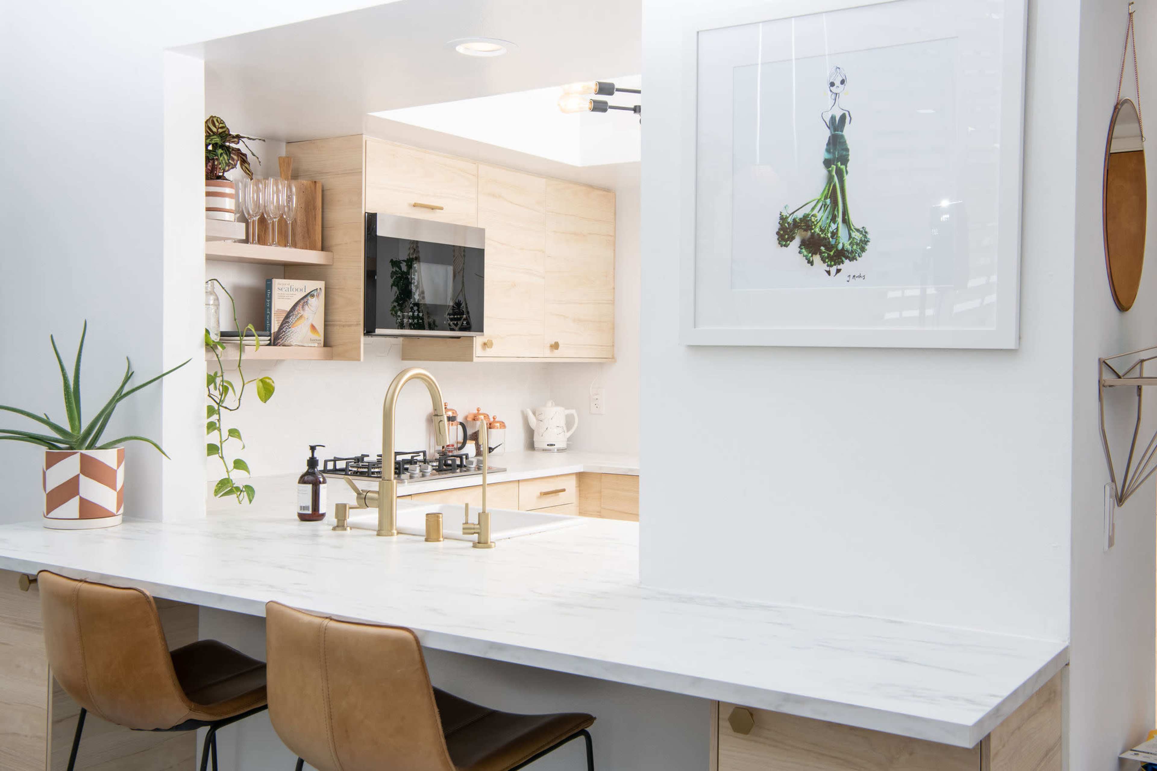A modern kitchen features a marble countertop, bar stools, and a framed artwork on the wall, with wooden cabinetry and a gas stove visible in the background.