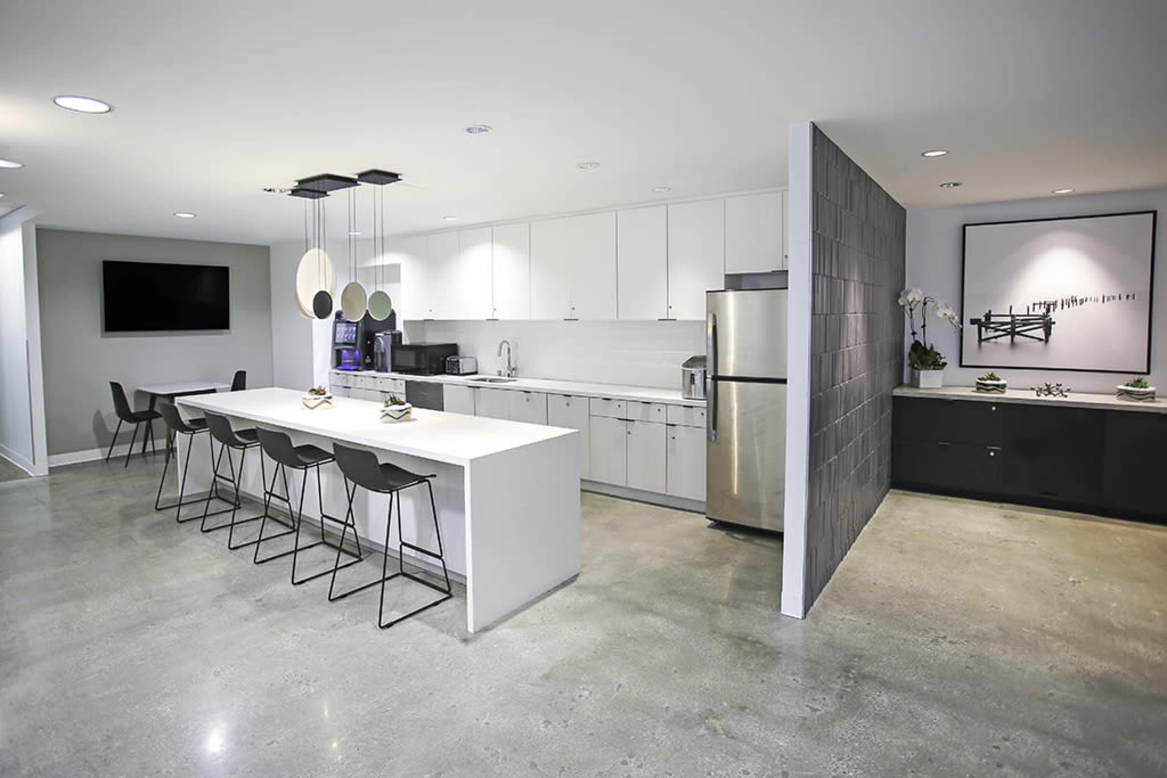 A modern kitchen features white cabinetry, a central island with bar seating, stainless steel appliances, and polished concrete flooring.