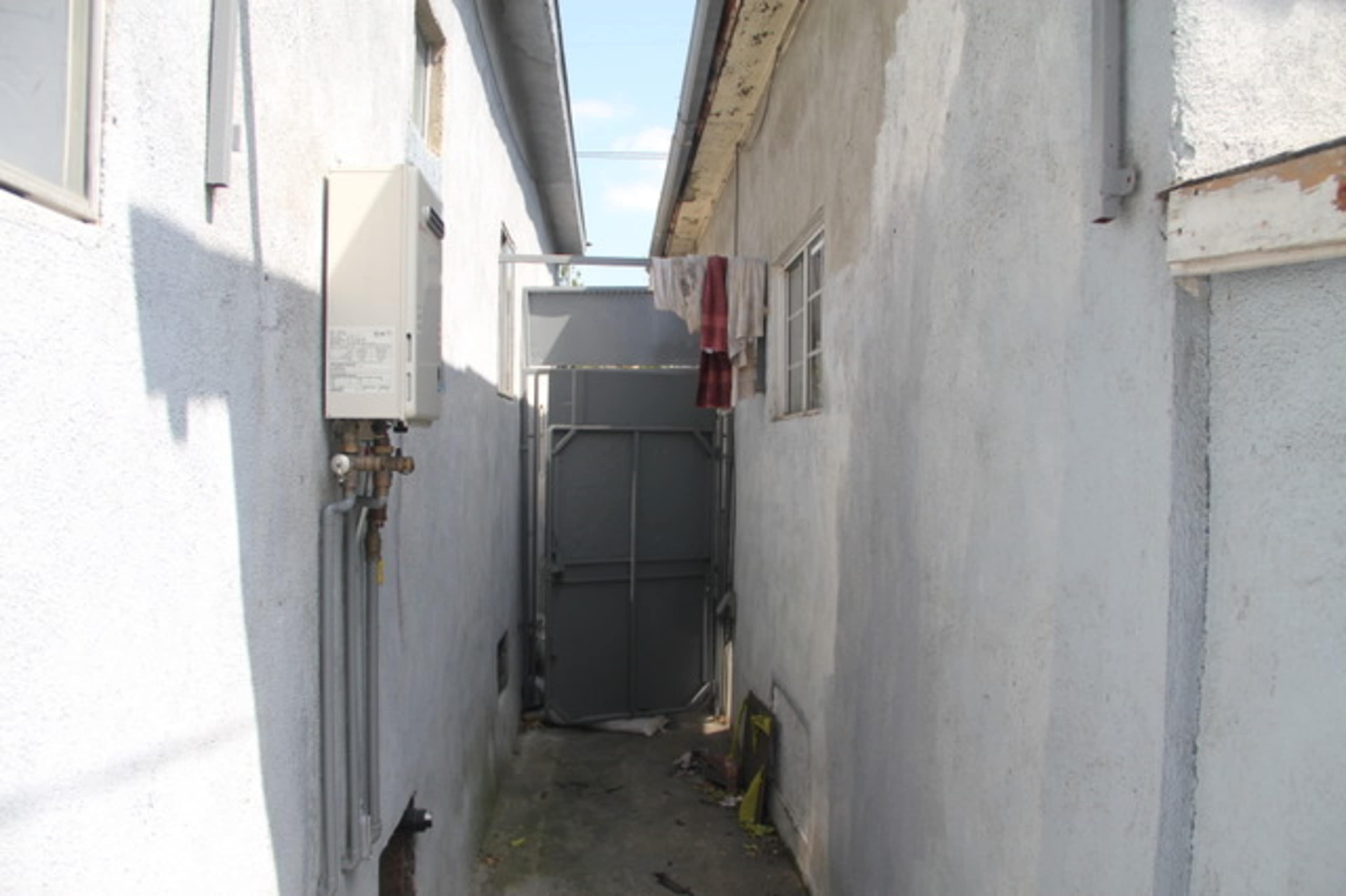A narrow alleyway between two buildings, with a gray gate at the end and clothes hanging on a line.