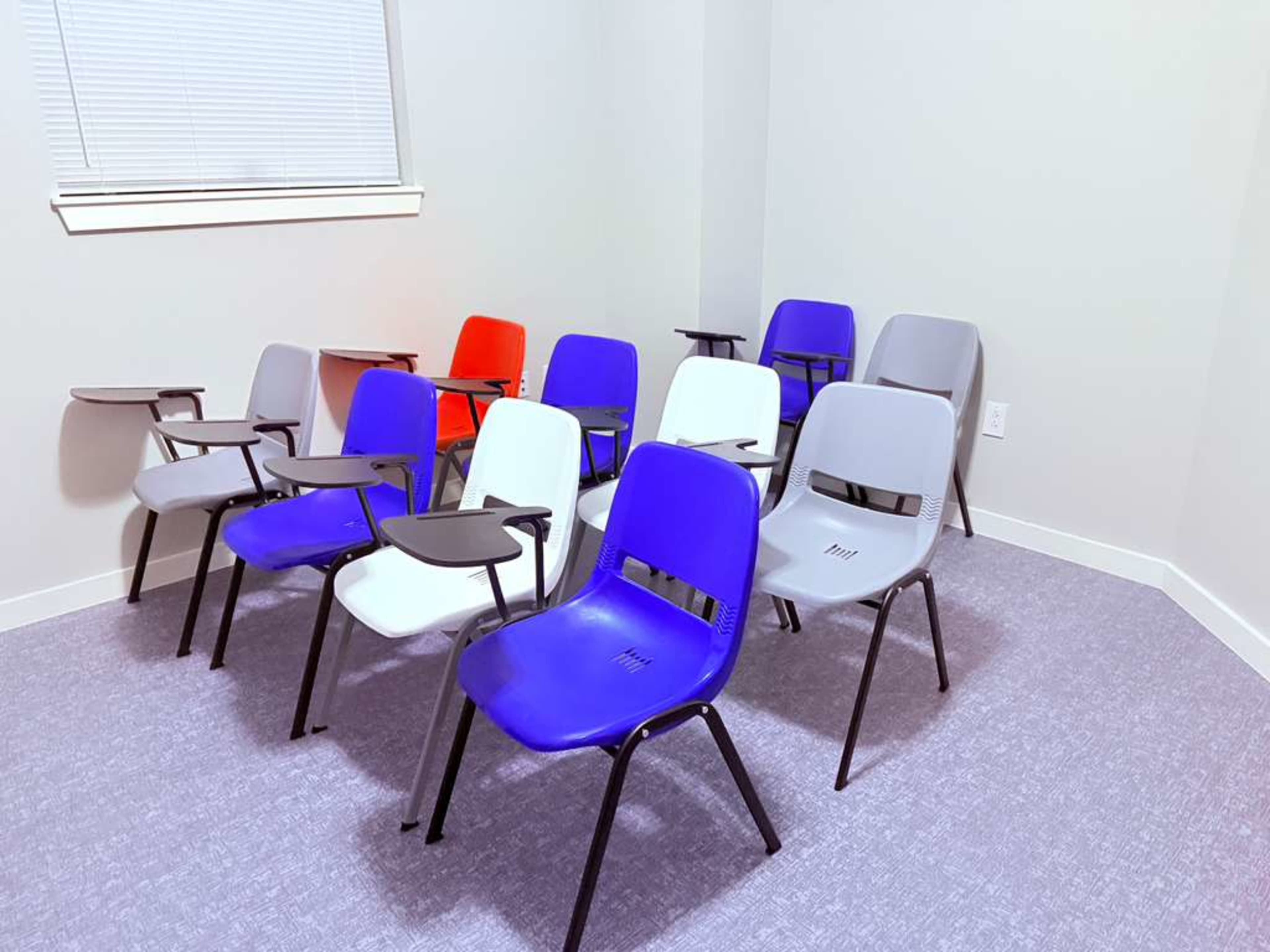 A room contains several chairs in various colors, arranged with some facing forward and others slightly angled.