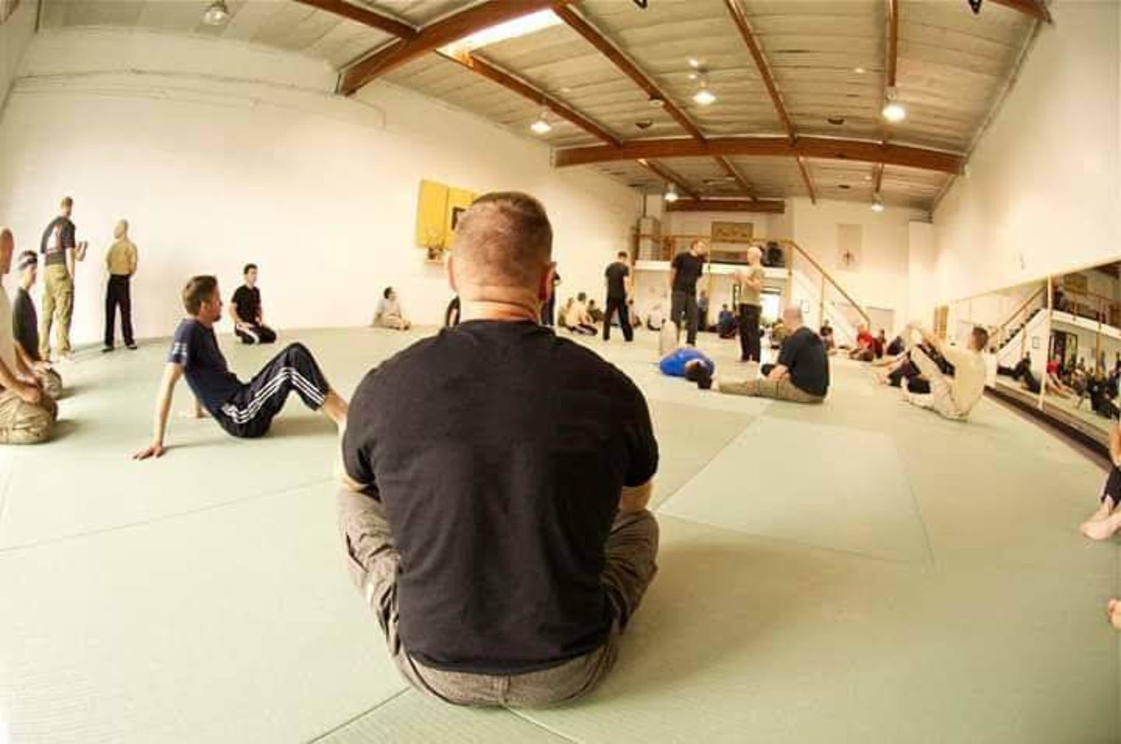 A group of people practices martial arts on mats in a spacious training facility.