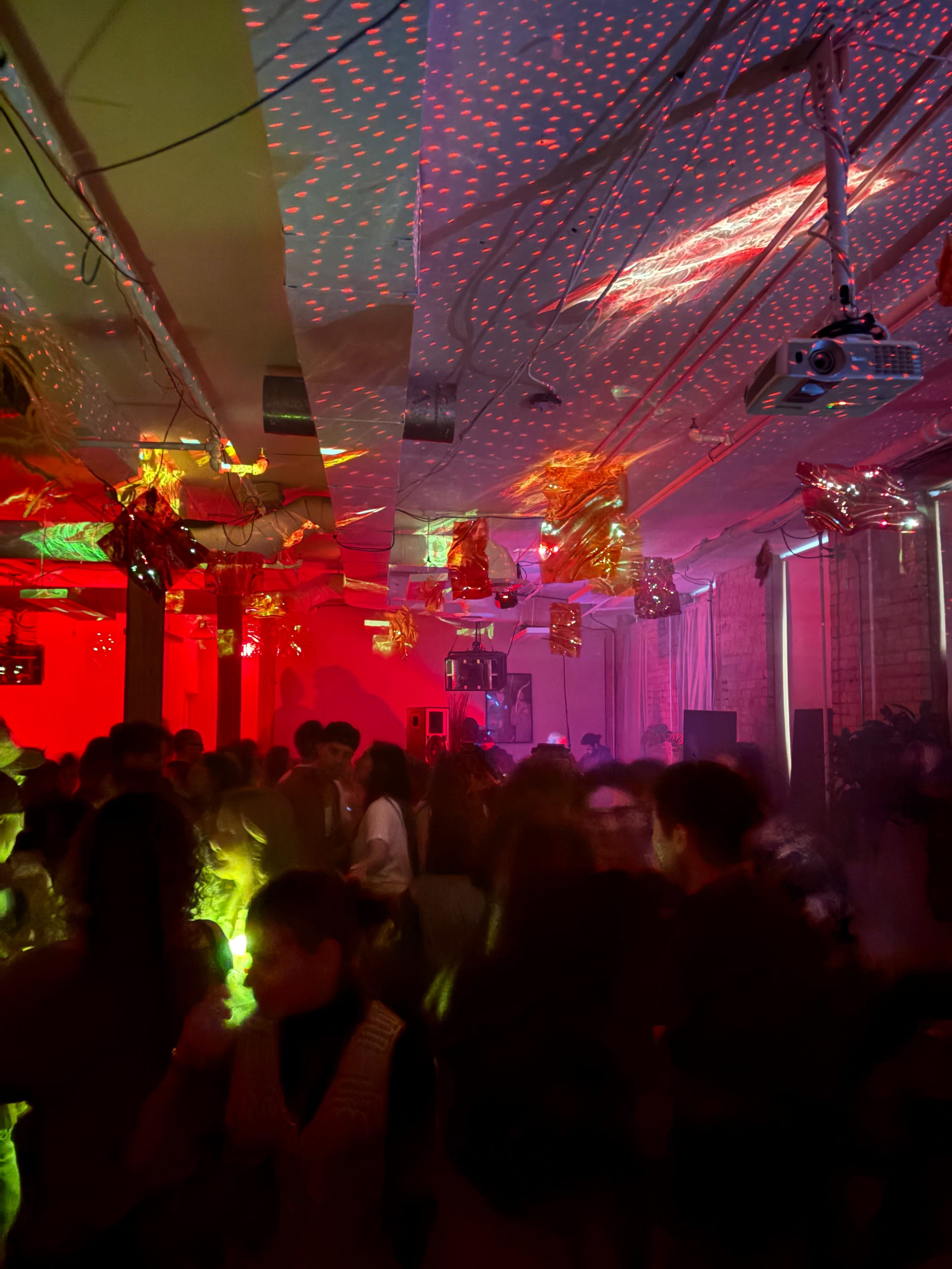 A crowded party scene with colorful lights and projections illuminating the space.
