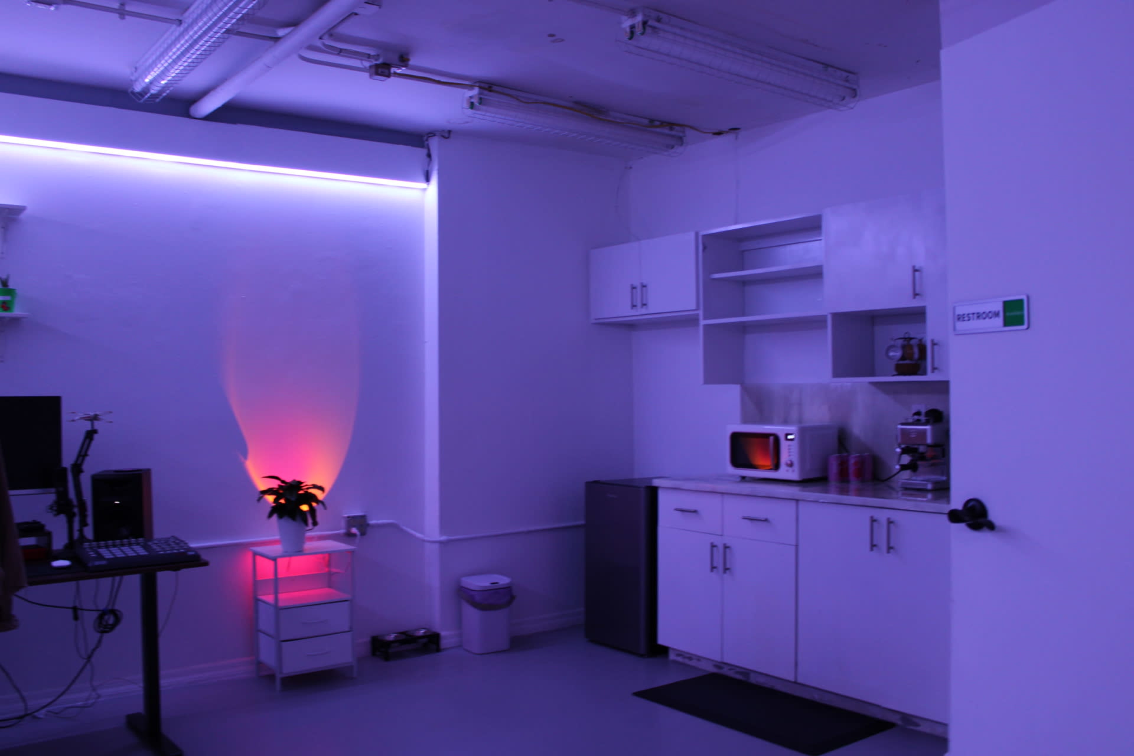 The image shows a modern kitchen area with white cabinets and appliances, illuminated by purple ambient lighting.