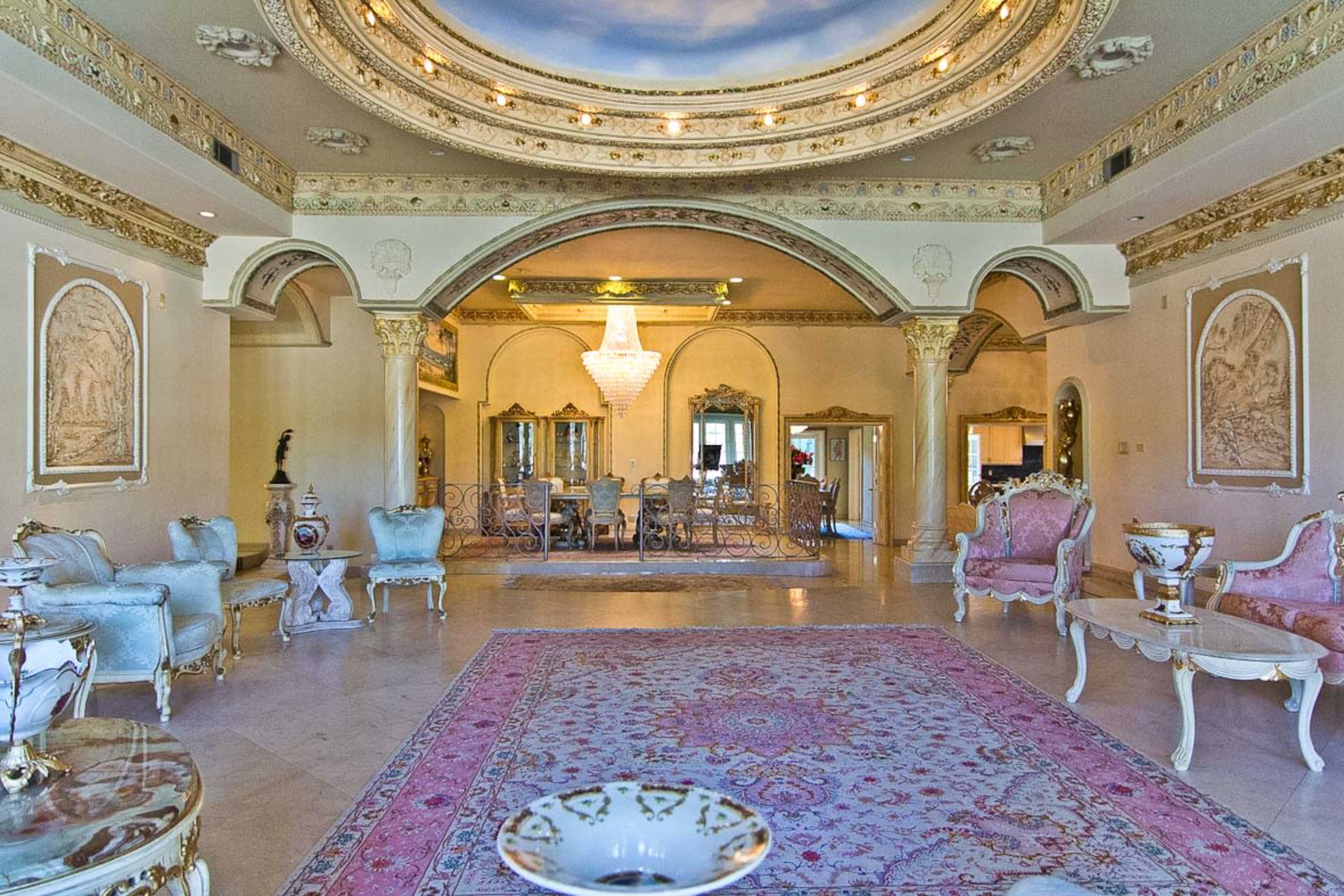 An elaborately decorated living room with ornate furnishings, a large chandelier, and a central area rug.