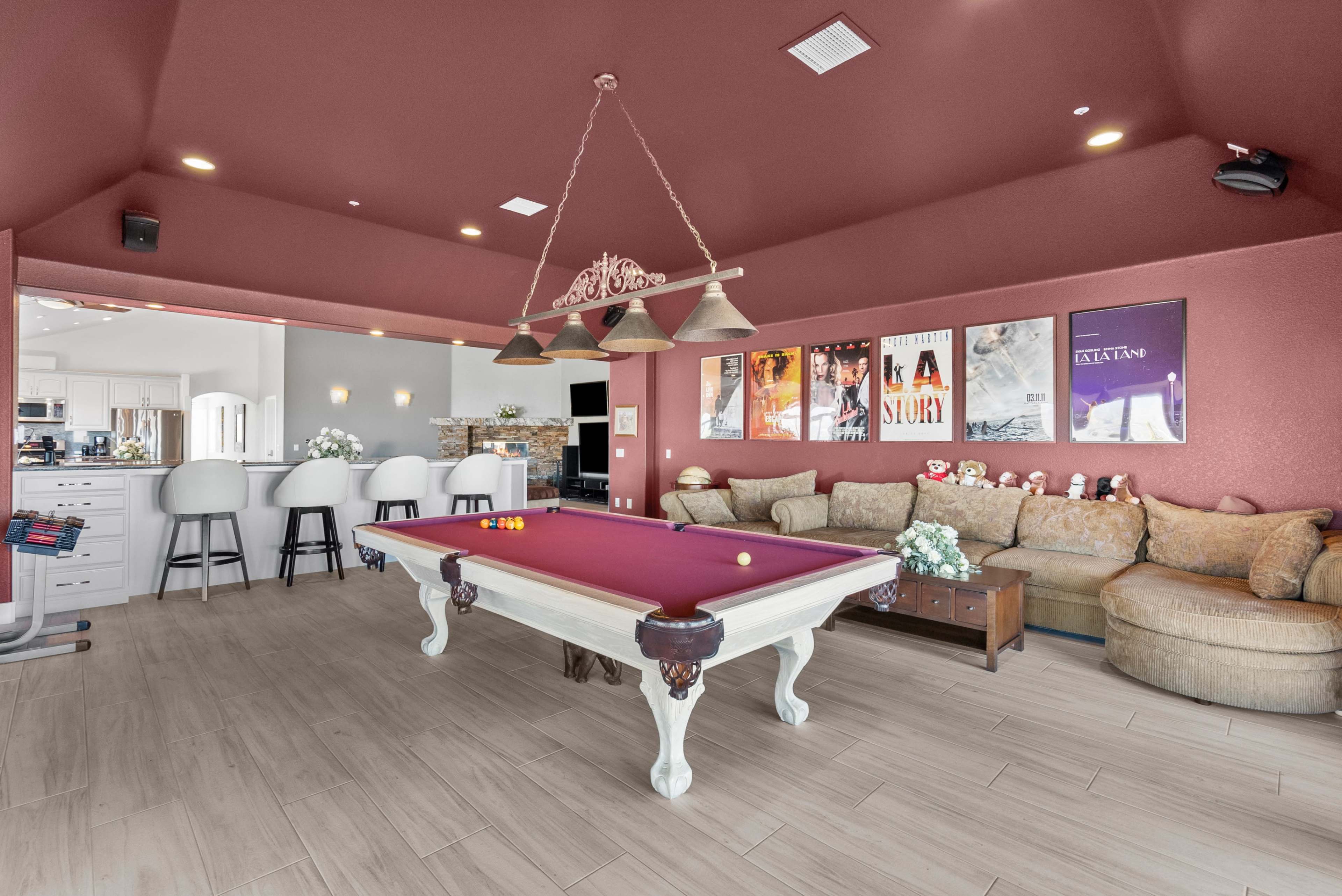 A spacious game room features a billiard table, a large sectional sofa, and movie posters on the walls.
