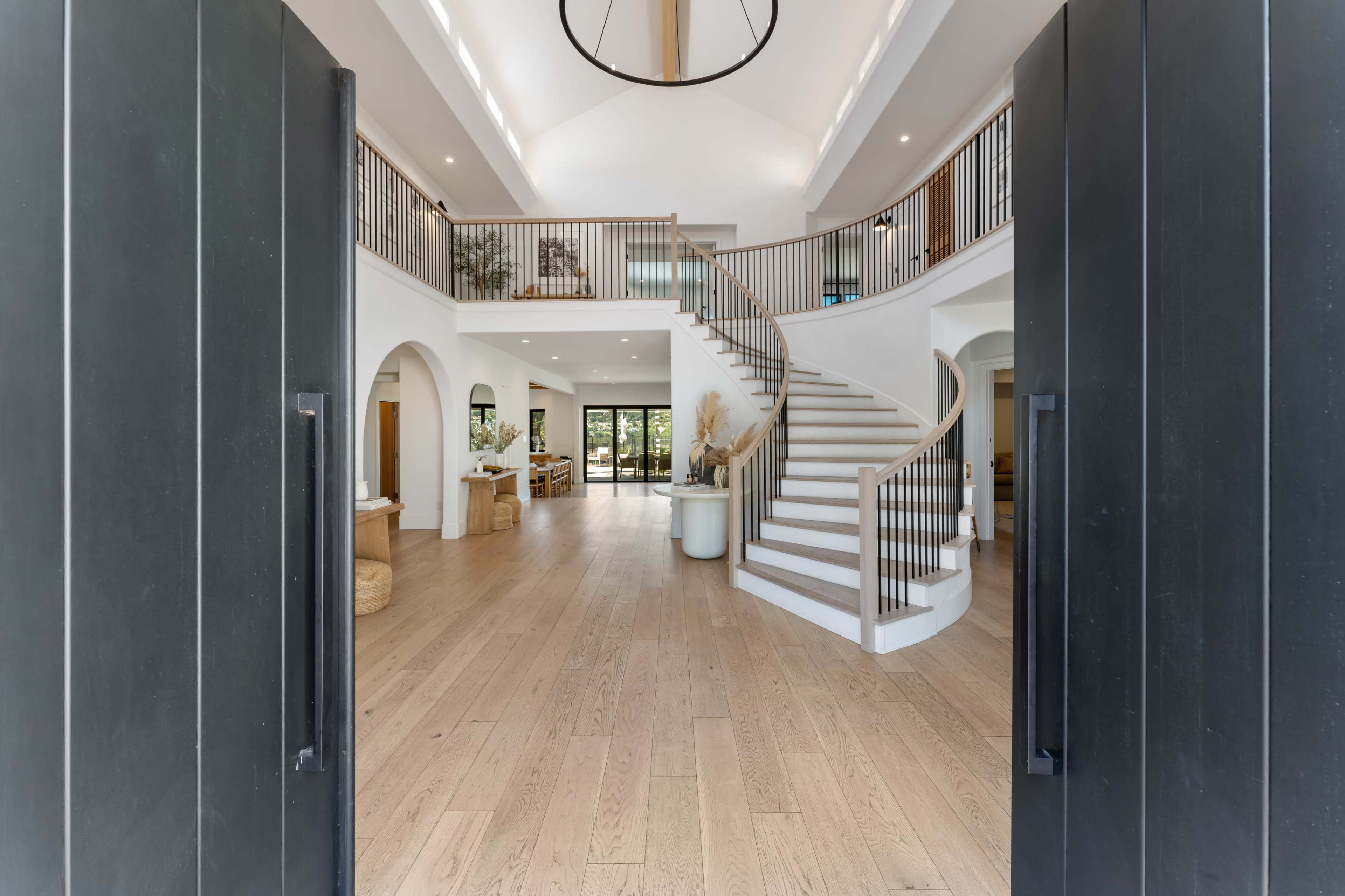 A spacious entrance hall with a sweeping staircase and large windows that open to a view of the outdoors.