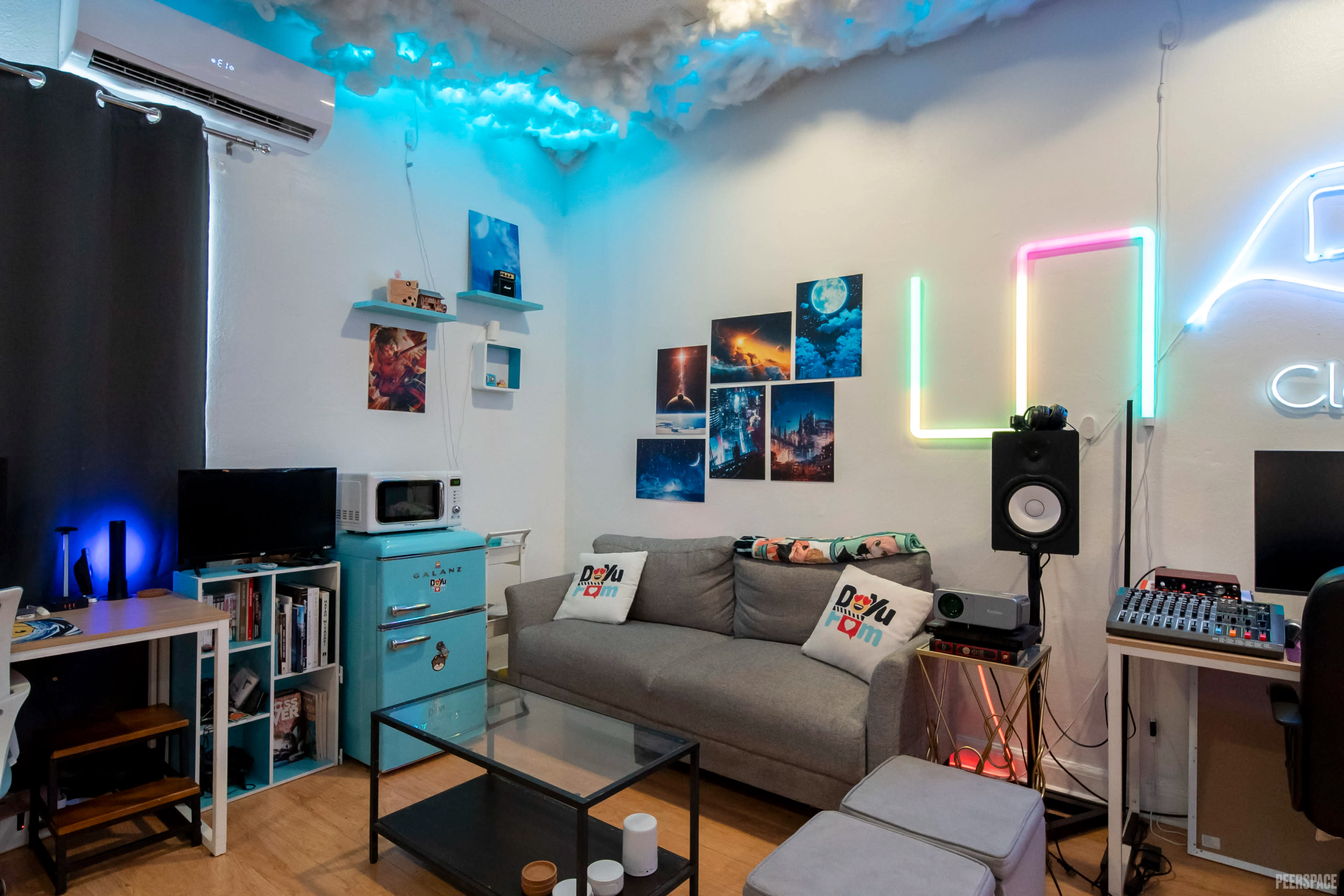 The image shows a cozy living room with a gray sofa, colorful wall art, a glass coffee table, and various electronic gadgets arranged around the space.
