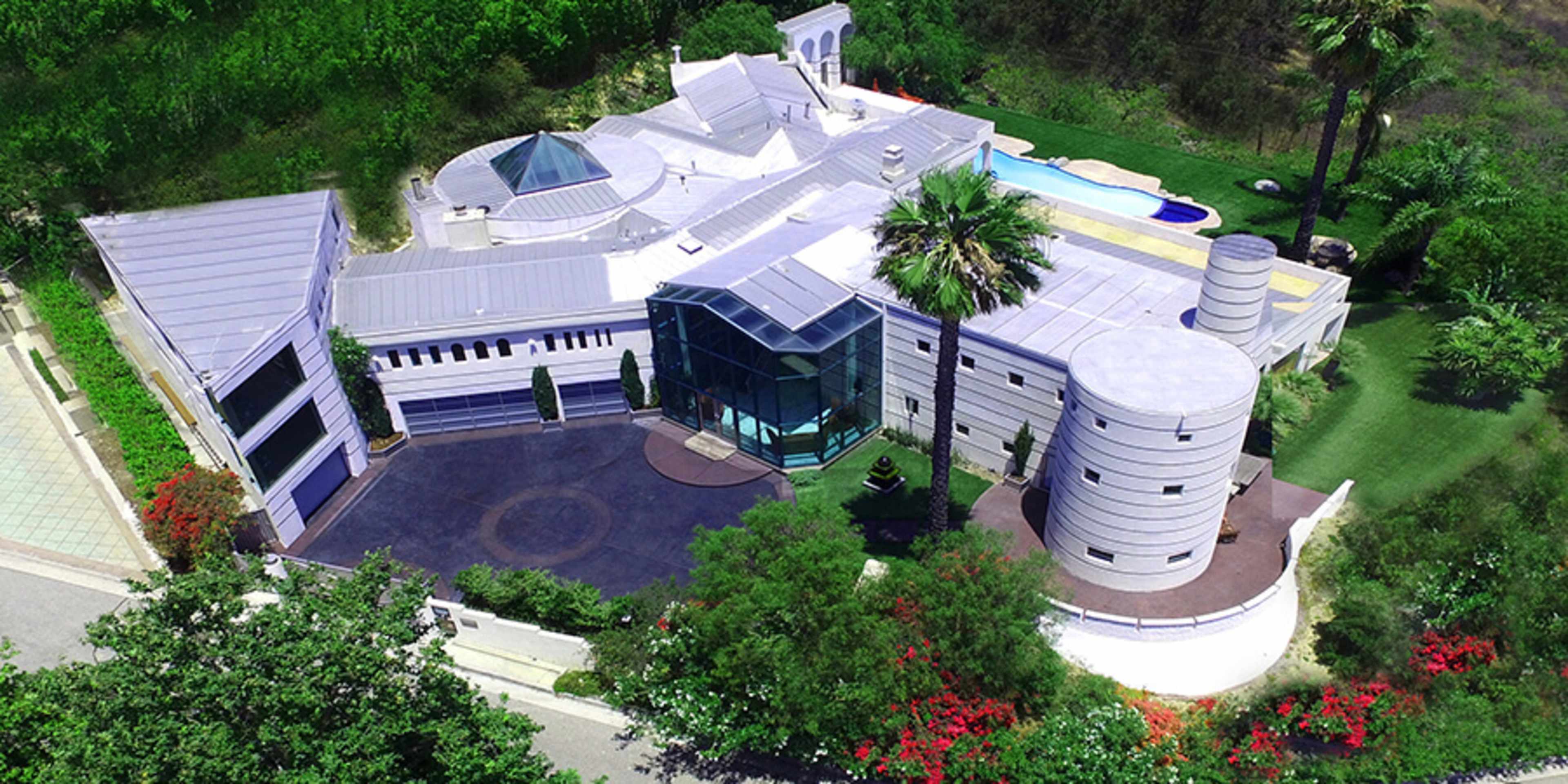 A large, modern house with a unique architectural design, surrounded by greenery and featuring a swimming pool.