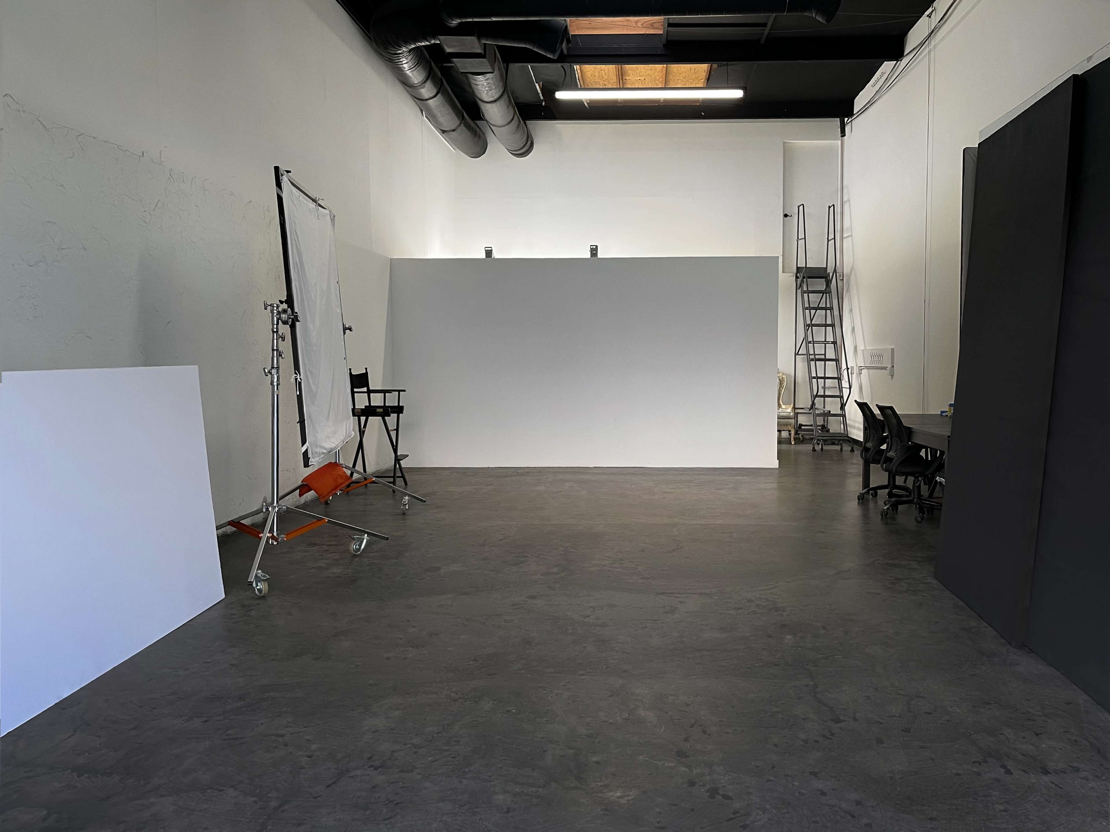 A spacious studio with a large empty backdrop, a few chairs, and a ladder against the wall.
