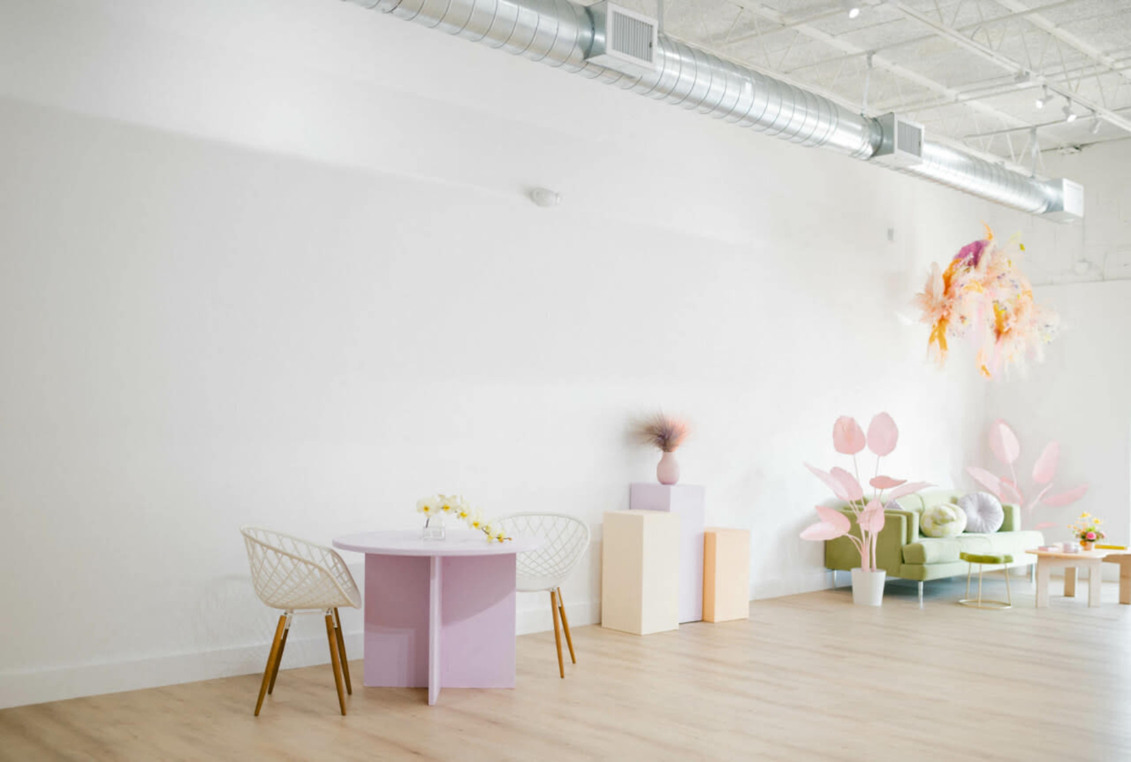 A spacious, minimalist interior featuring a round table and chairs, a green sofa, and decorative elements on a white wall.